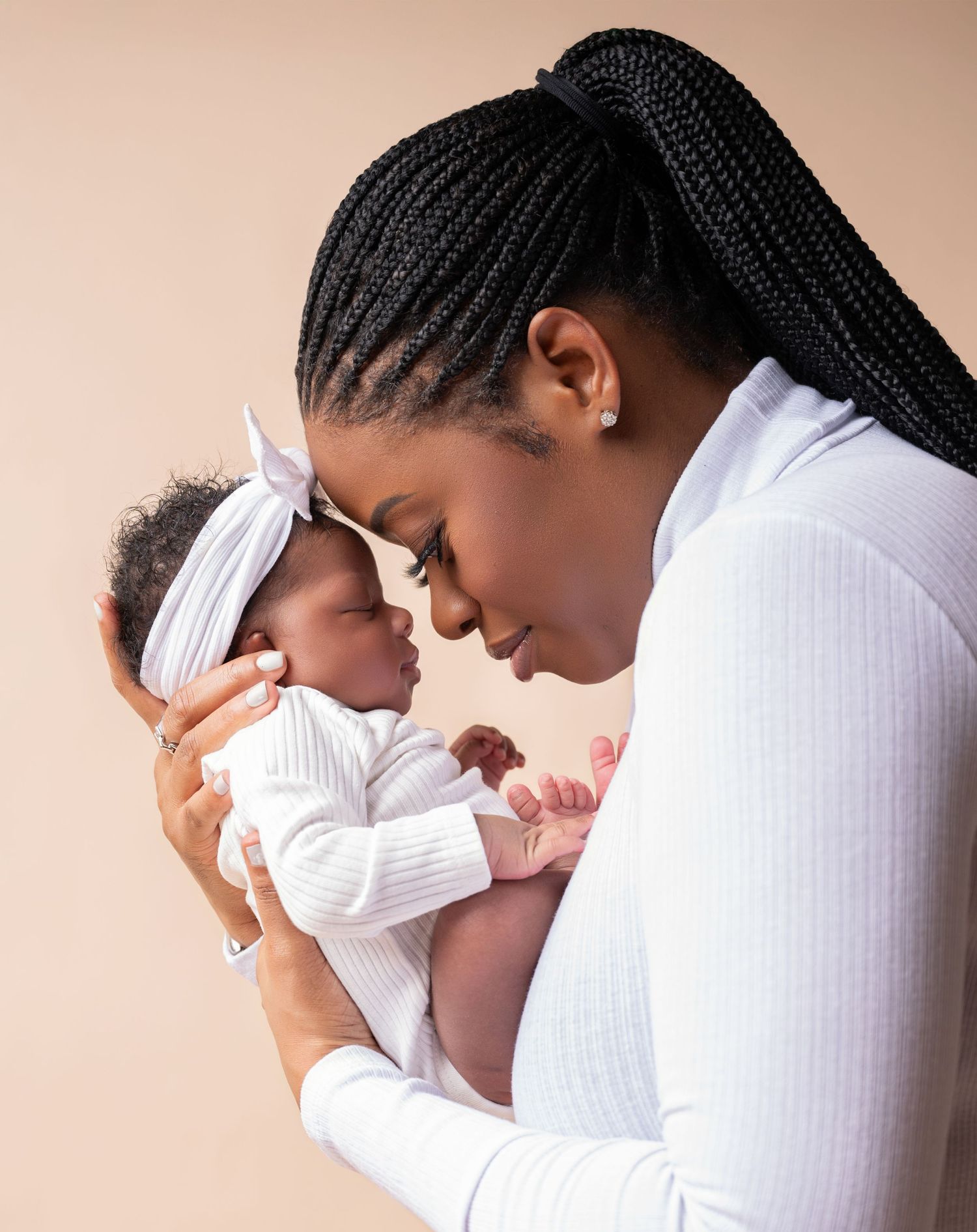 A tender moment between parent and baby in white outfits against a neutral backdrop.