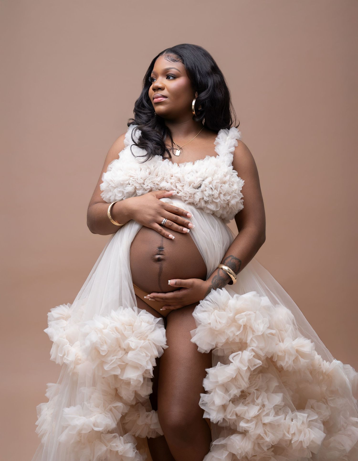 Artistic maternity photoshoot featuring elegant white ruffled dress against neutral beige background.