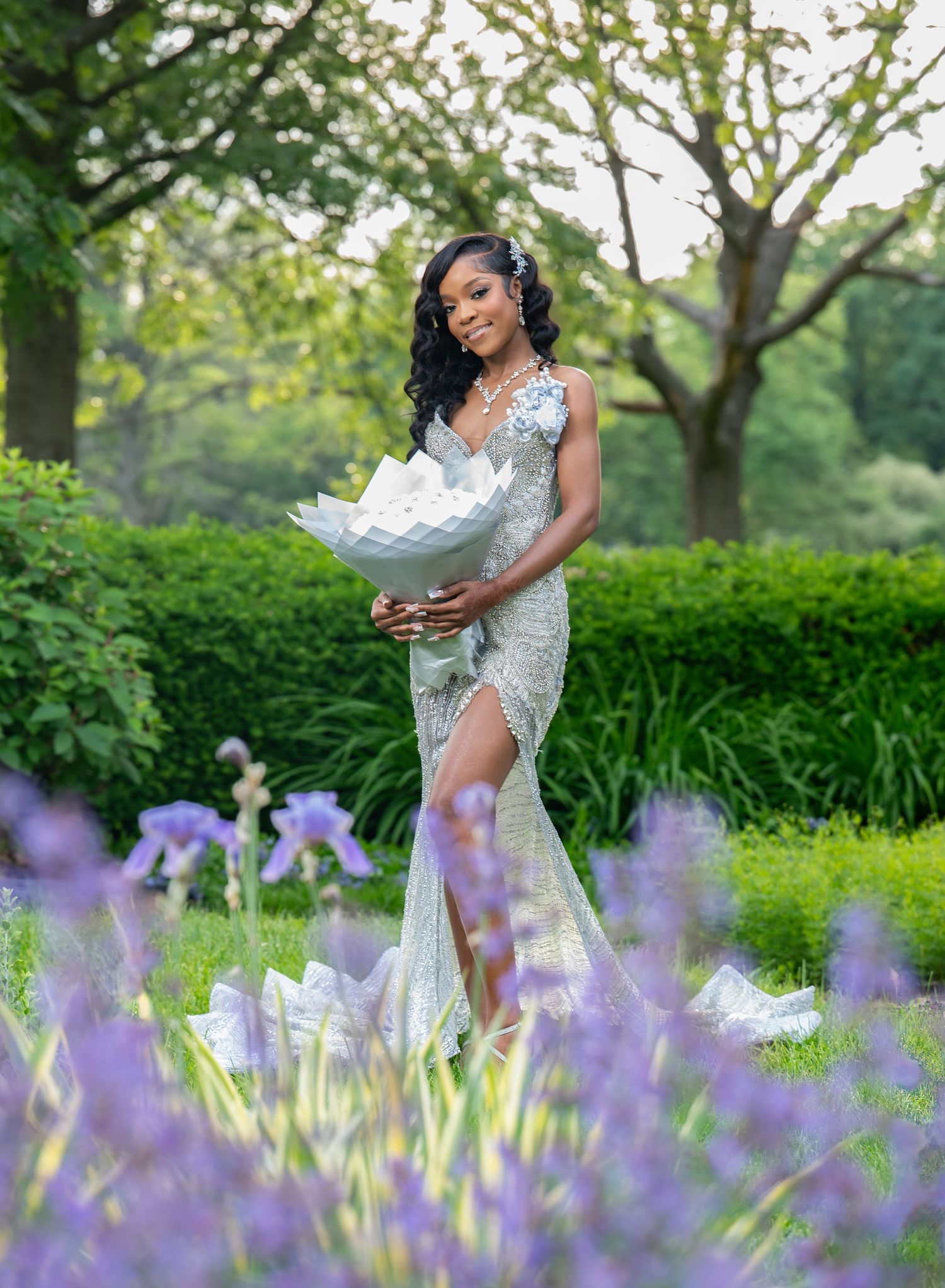A figure in white poses gracefully among blooming purple lavender flowers in a lush garden setting.