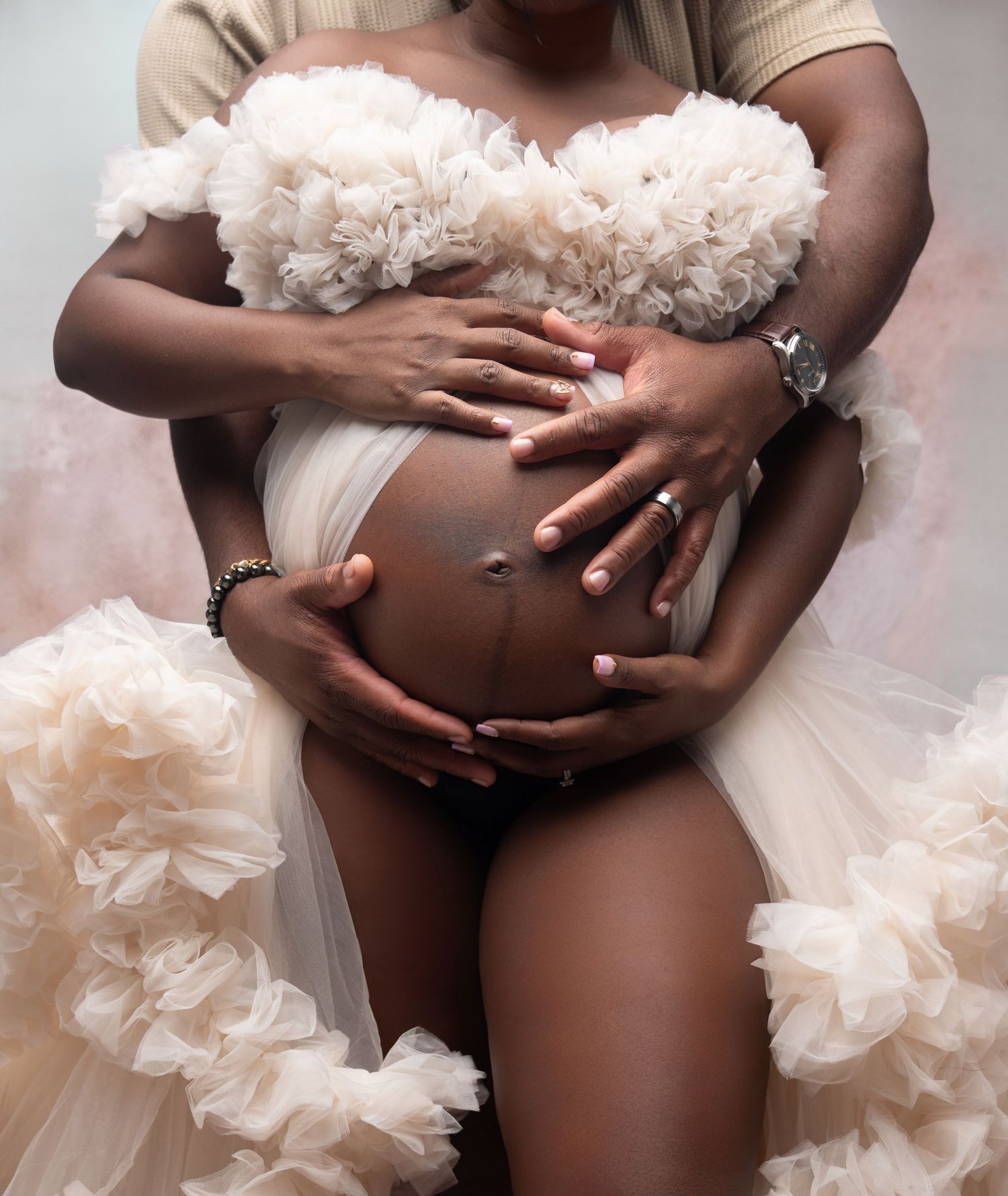 Artistic maternity photo showing hands cradling a pregnant belly surrounded by soft pink tulle fabric details.