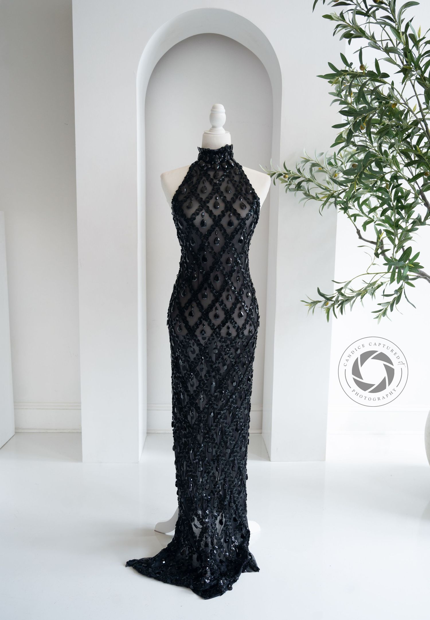 A sleek black sequined high-neck evening gown with diamond pattern design displayed on a white mannequin in an arched alcove.