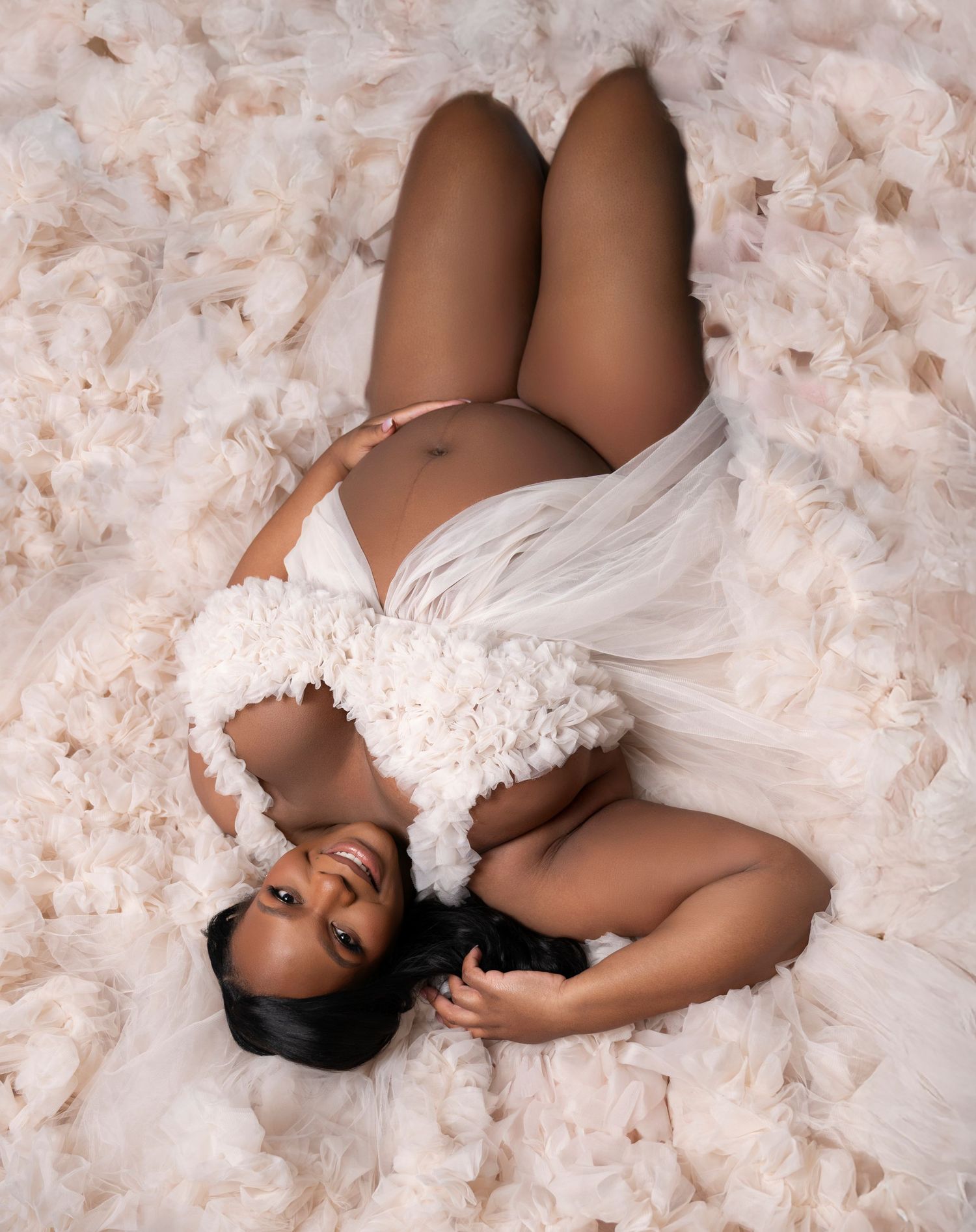 A figure in white lace lies gracefully on a blush pink textured backdrop in an artistic boudoir series.