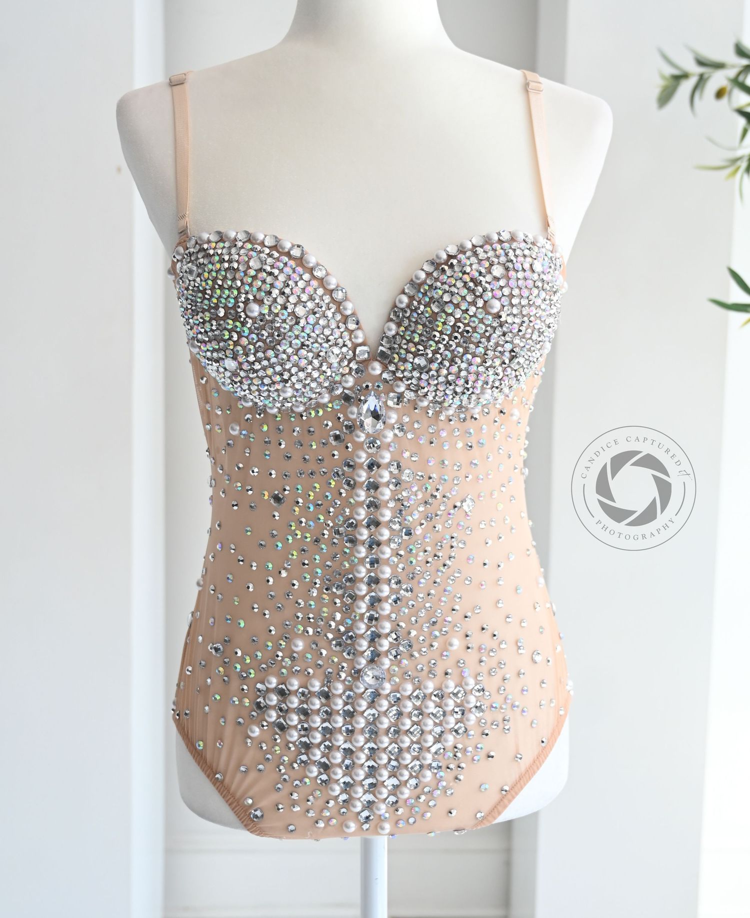 Nude-colored corset bodysuit embellished with crystal rhinestones in an intricate pattern on display against white background.