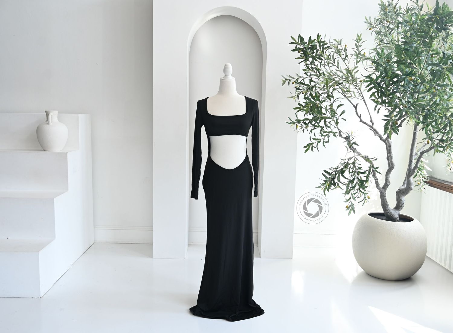A minimalist lifestyle scene with a black dress form against a white wall featuring delicate greenery decor.