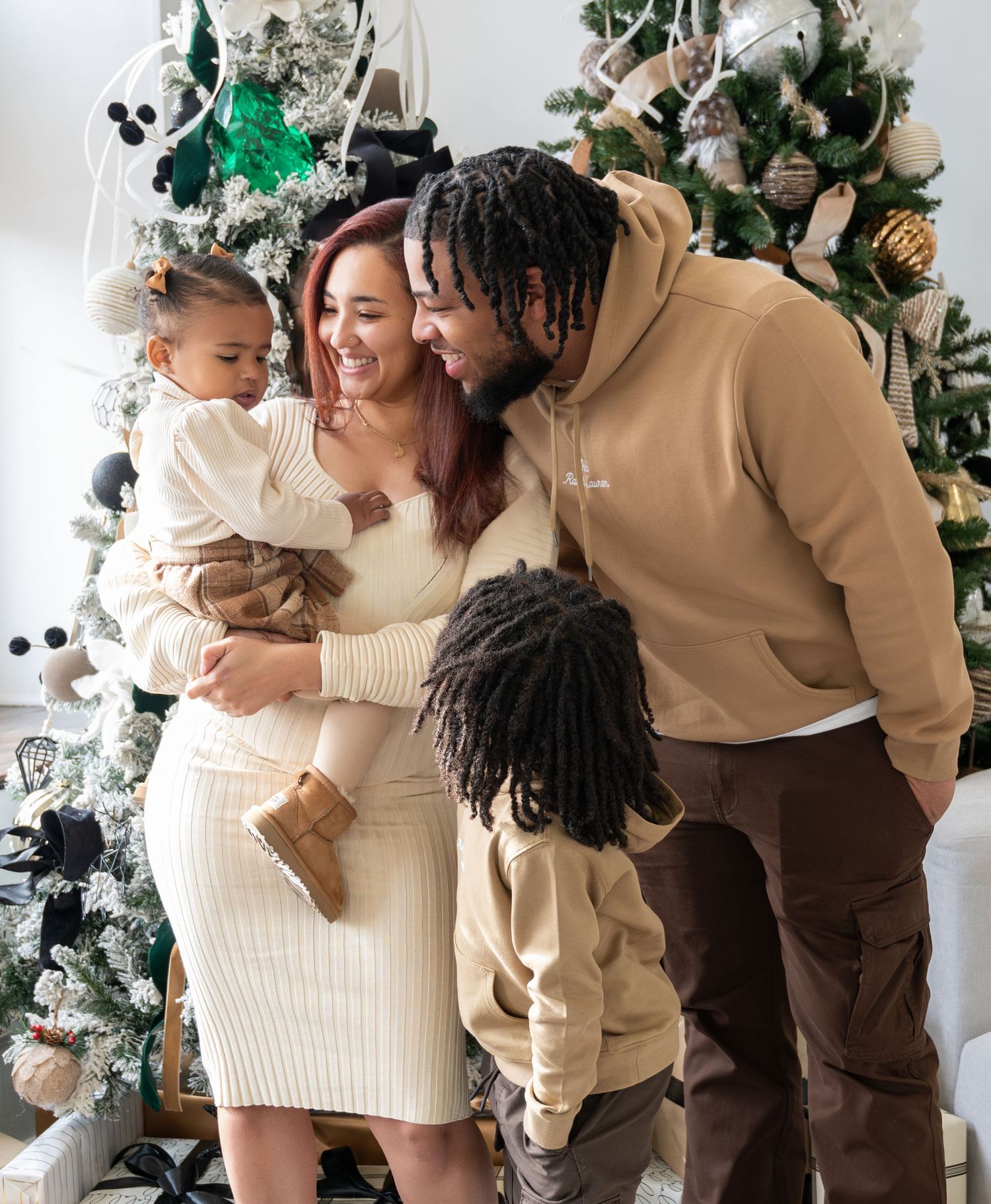 Family enjoying Christmas together by decorated tree in coordinating cream and brown outfits for Christmas mini sessions.