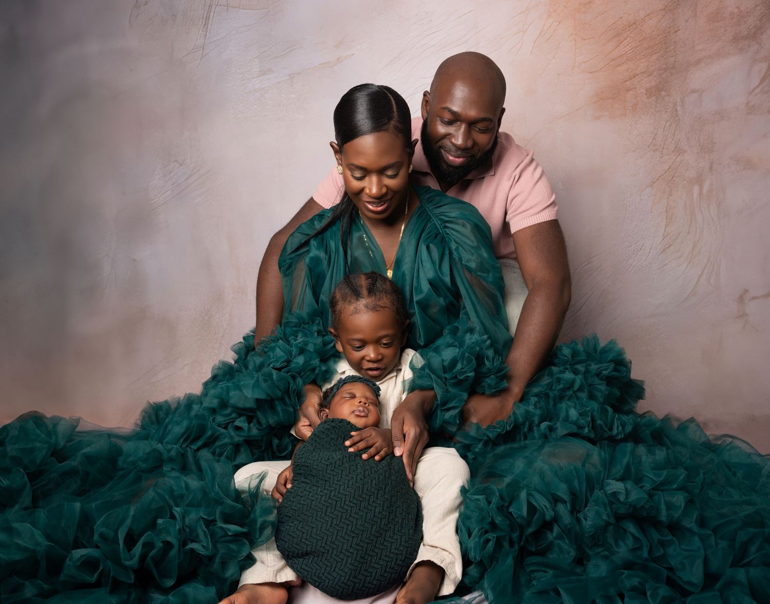 Family portrait of parents in teal ruffled attire holding a newborn and toddler in a studio setting.