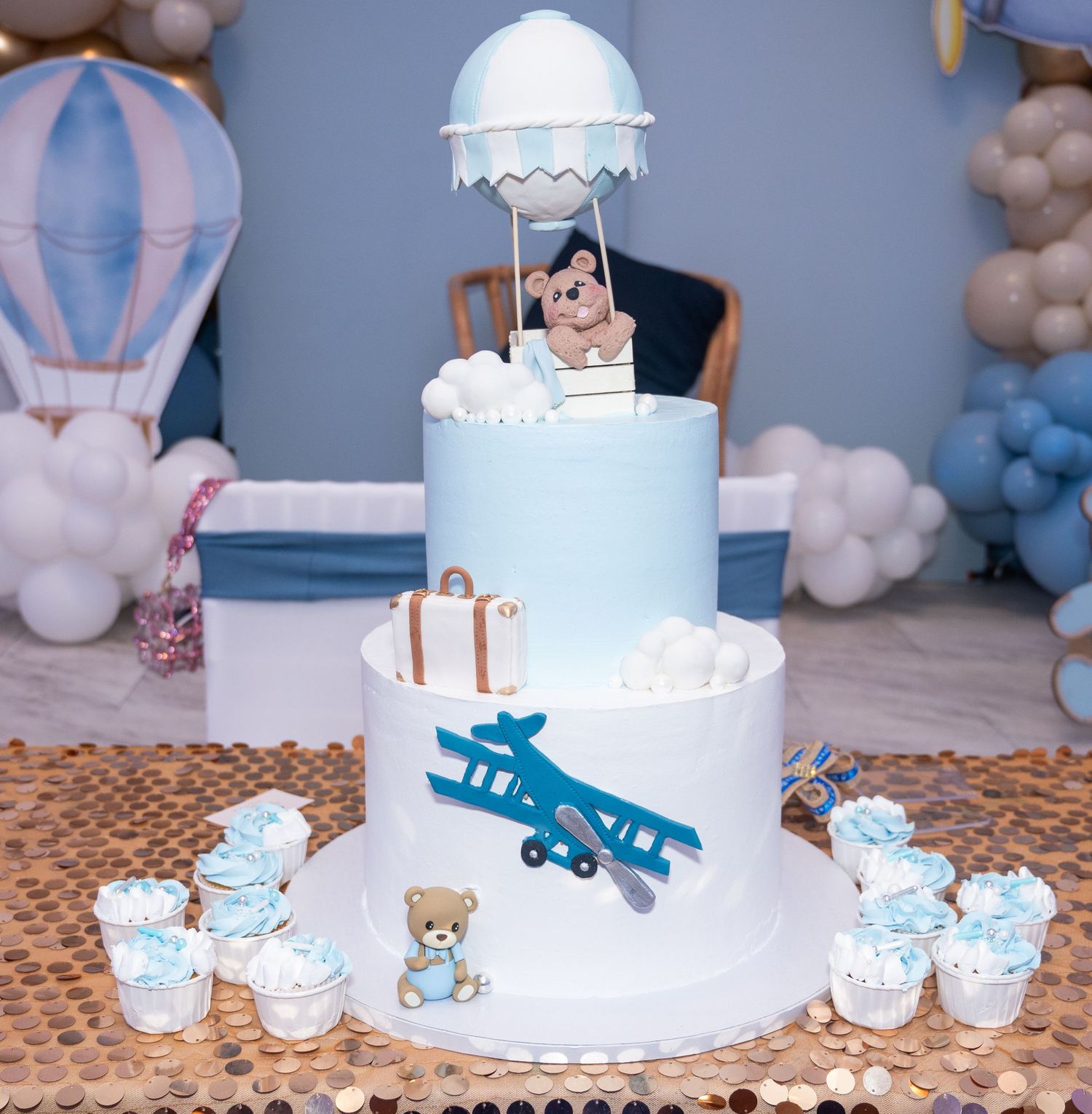 Light blue aviation themed baby shower cake with hot air balloon decorations and matching cupcakes.