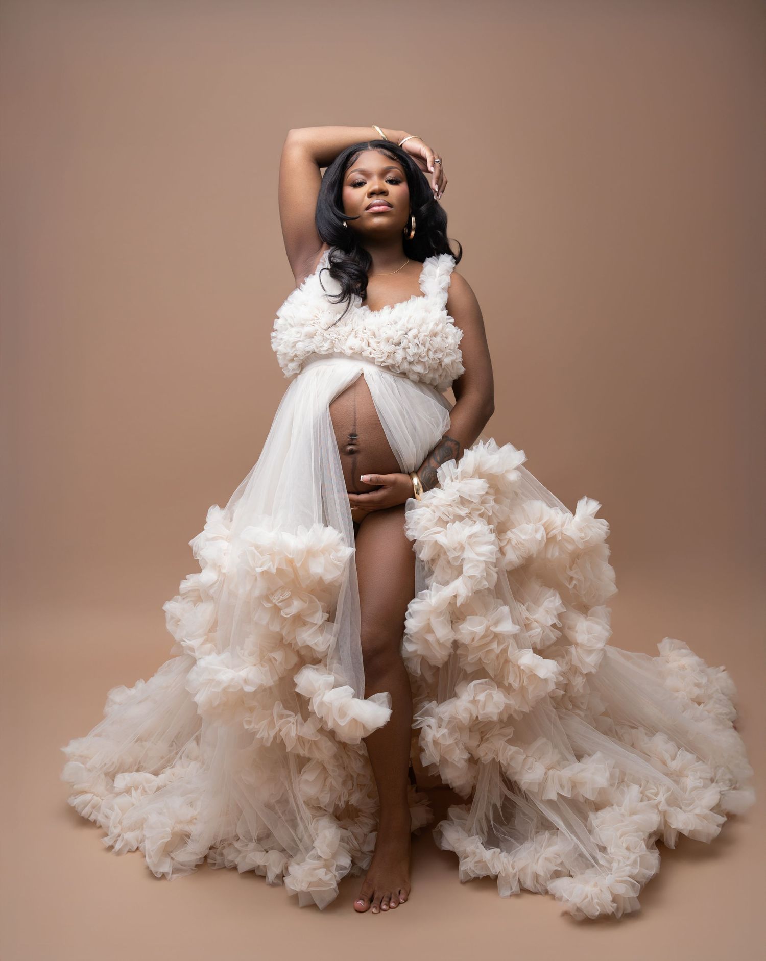 Elegant maternity photoshoot featuring flowing white tulle fabric and dramatic poses against a warm brown backdrop.