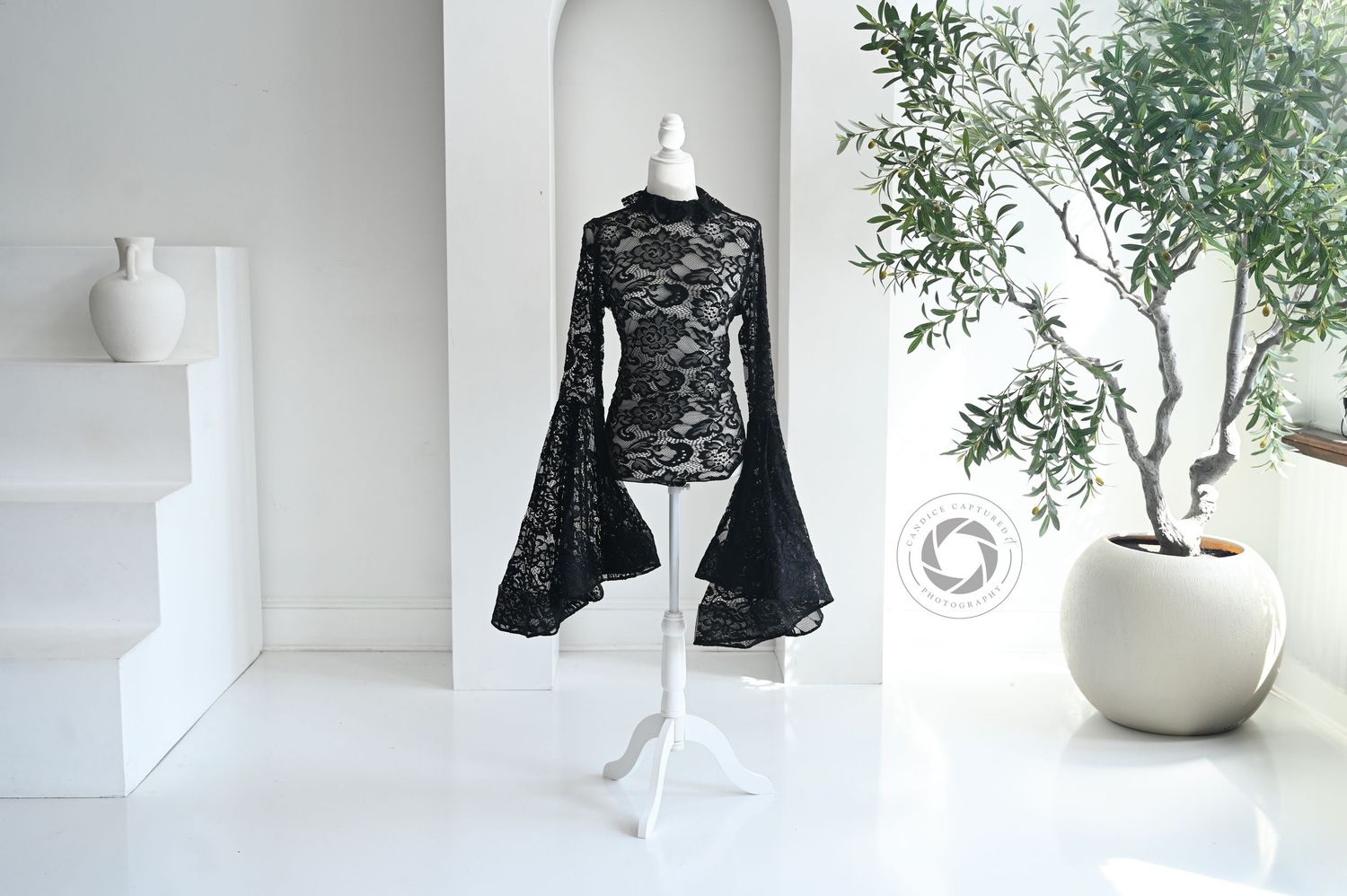 Stylish lace top and white ceramic vase with plant arranged in a modern minimalist interior setting.
