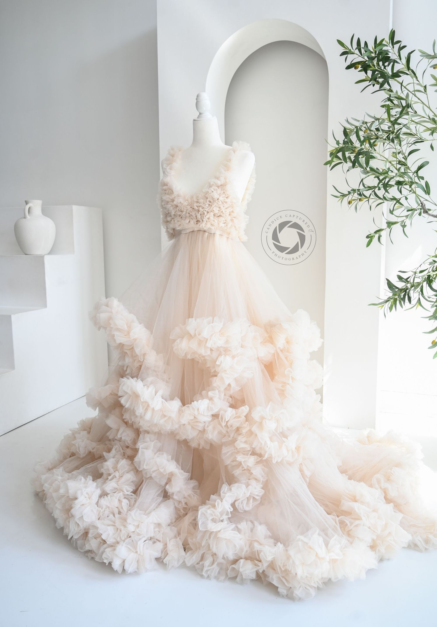 A blush pink tulle wedding dress with dramatic voluminous ruffles cascading down the skirt in an ethereal studio setting.