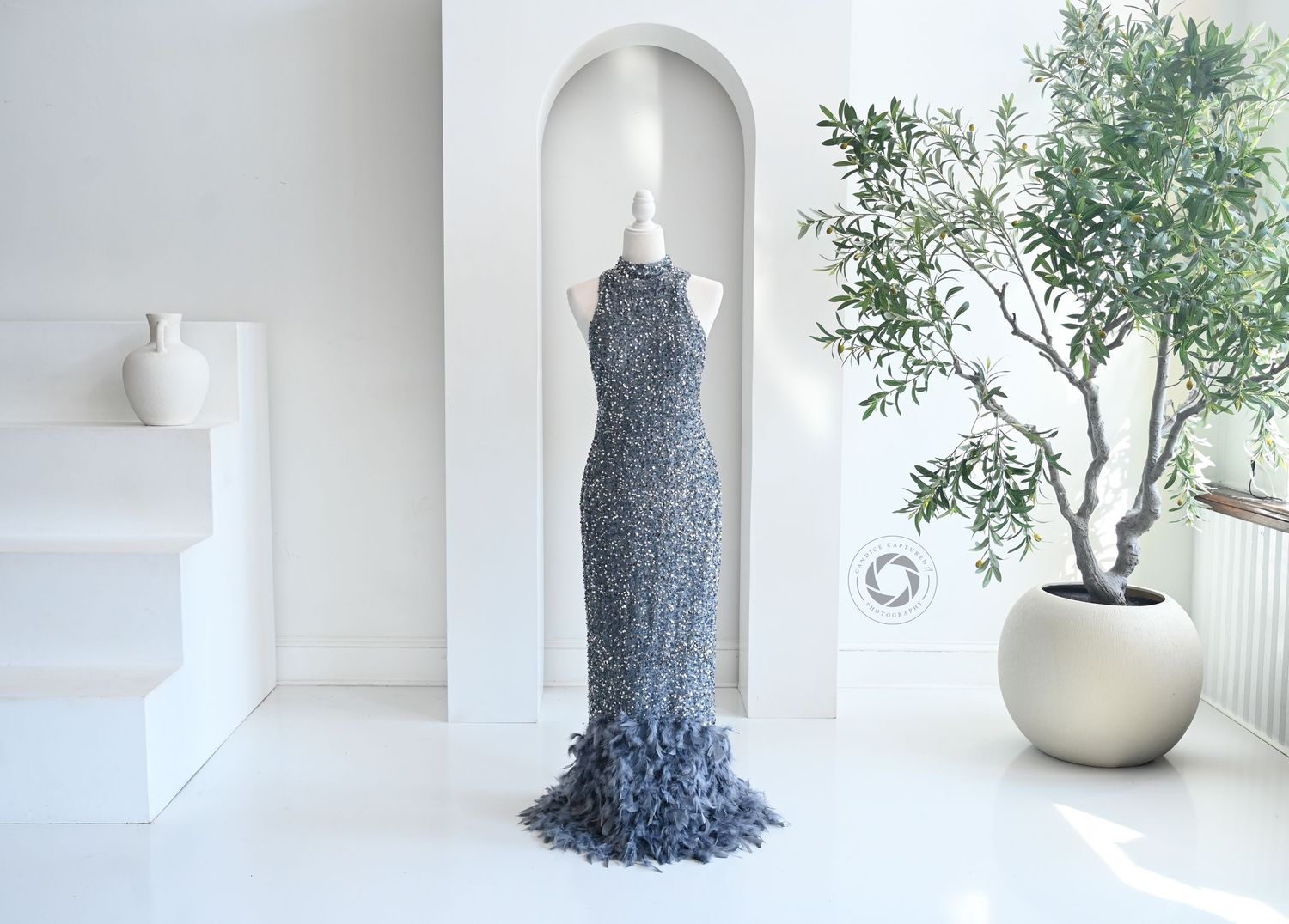 Minimalist white room interior featuring a contemporary gray tree sculpture and small potted plant against stark white walls.