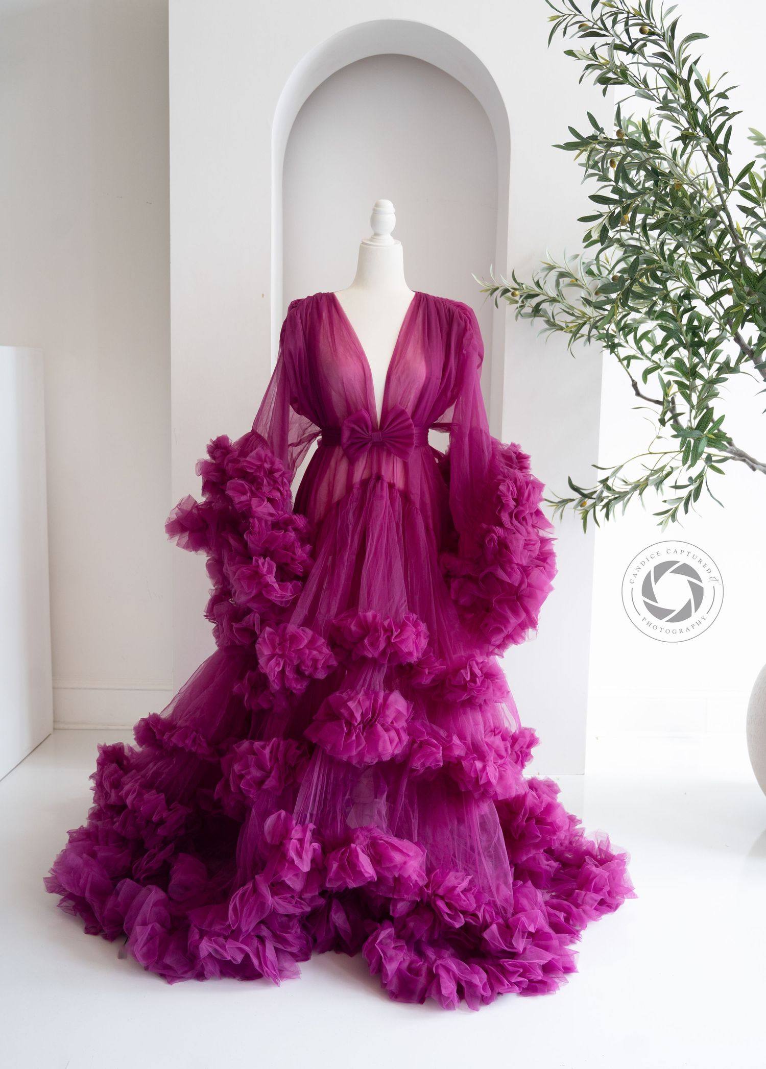 Luxurious magenta tulle robe with dramatic ruffled layers and sheer flowing sleeves displayed against white archway.