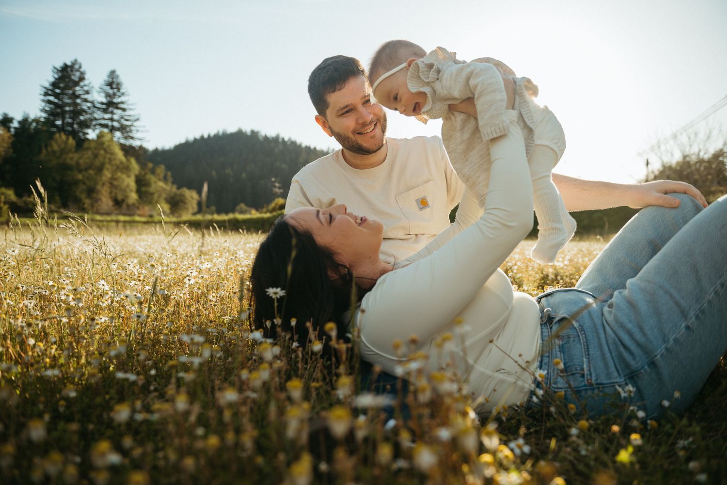 A couple embraces playfully in a golden sunlit meadow during a romantic outdoor photoshoot.