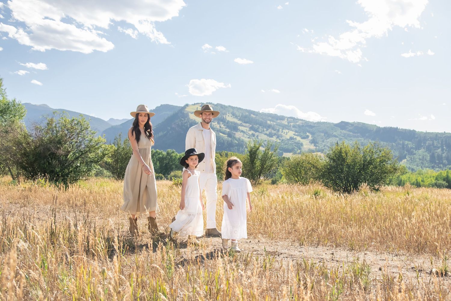 Fashionable family walking through a golden field with mountains in the background during a family photo session in Aspen Colorado