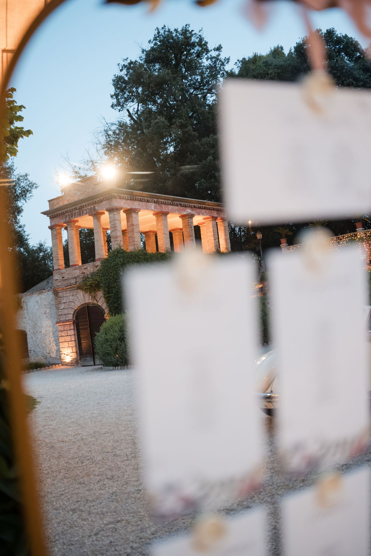 Elegant wedding seating chart display with blurred cards in foreground and illuminated classical pavilion at dusk.