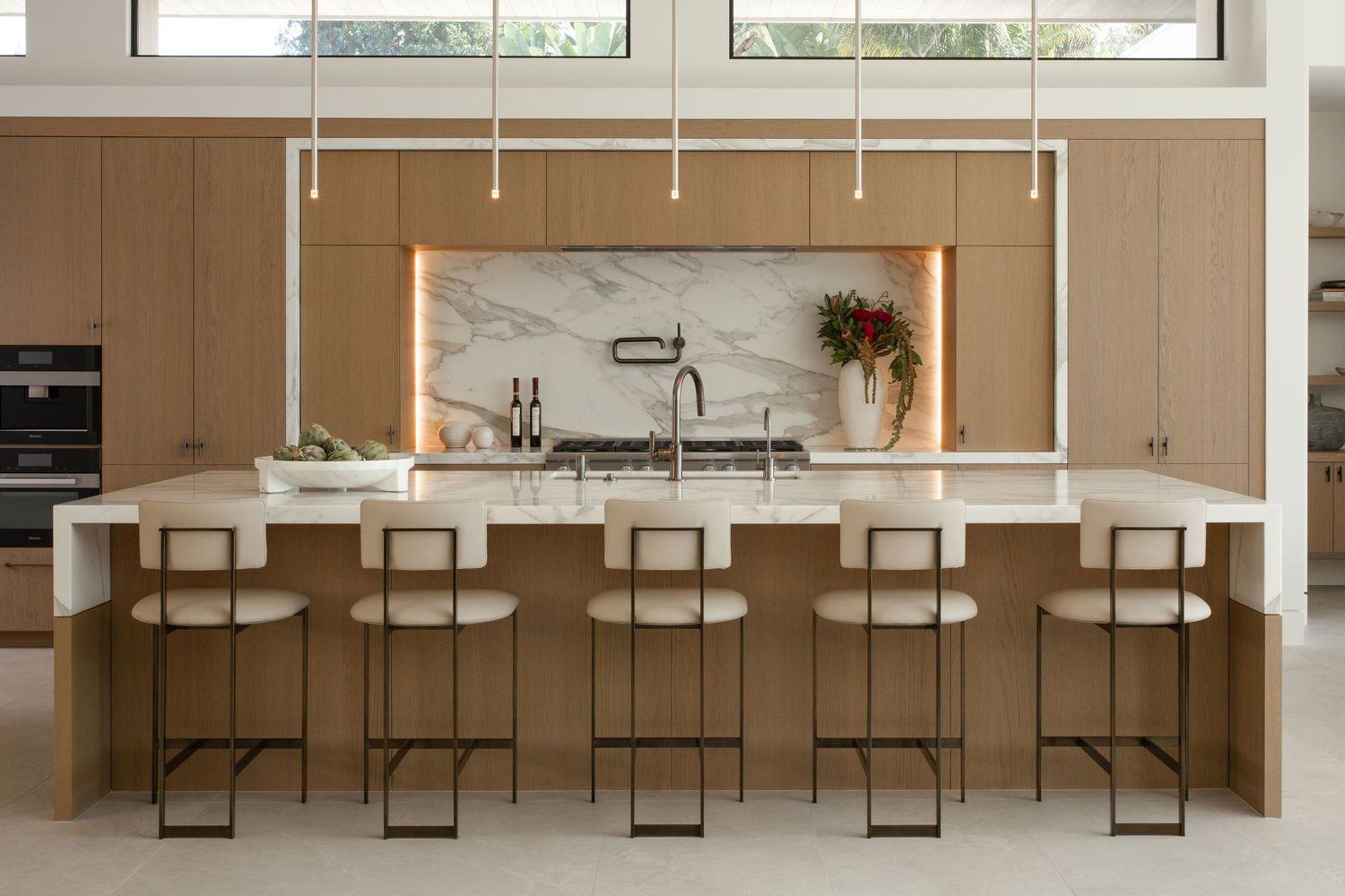 Contemporary dining room features a sleek long wooden table with black metal chairs and pendant lighting above.