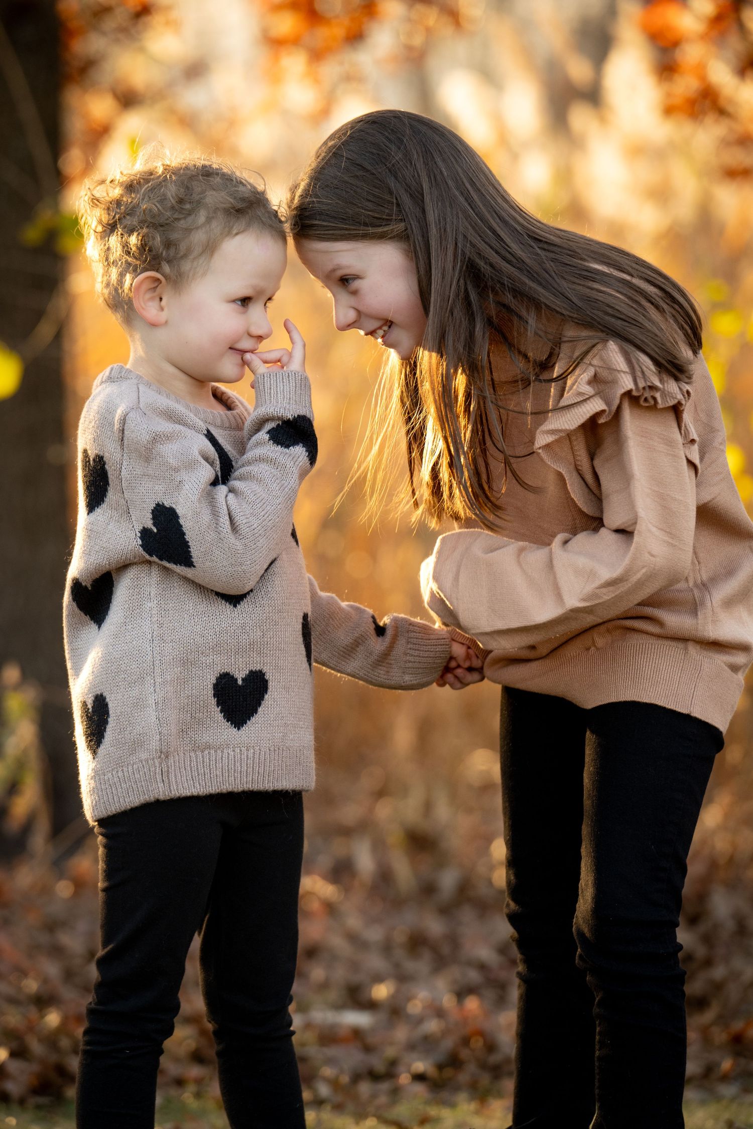 Two kids in sweaters share a sweet moment together while playing outdoors during golden hour autumn lighting.