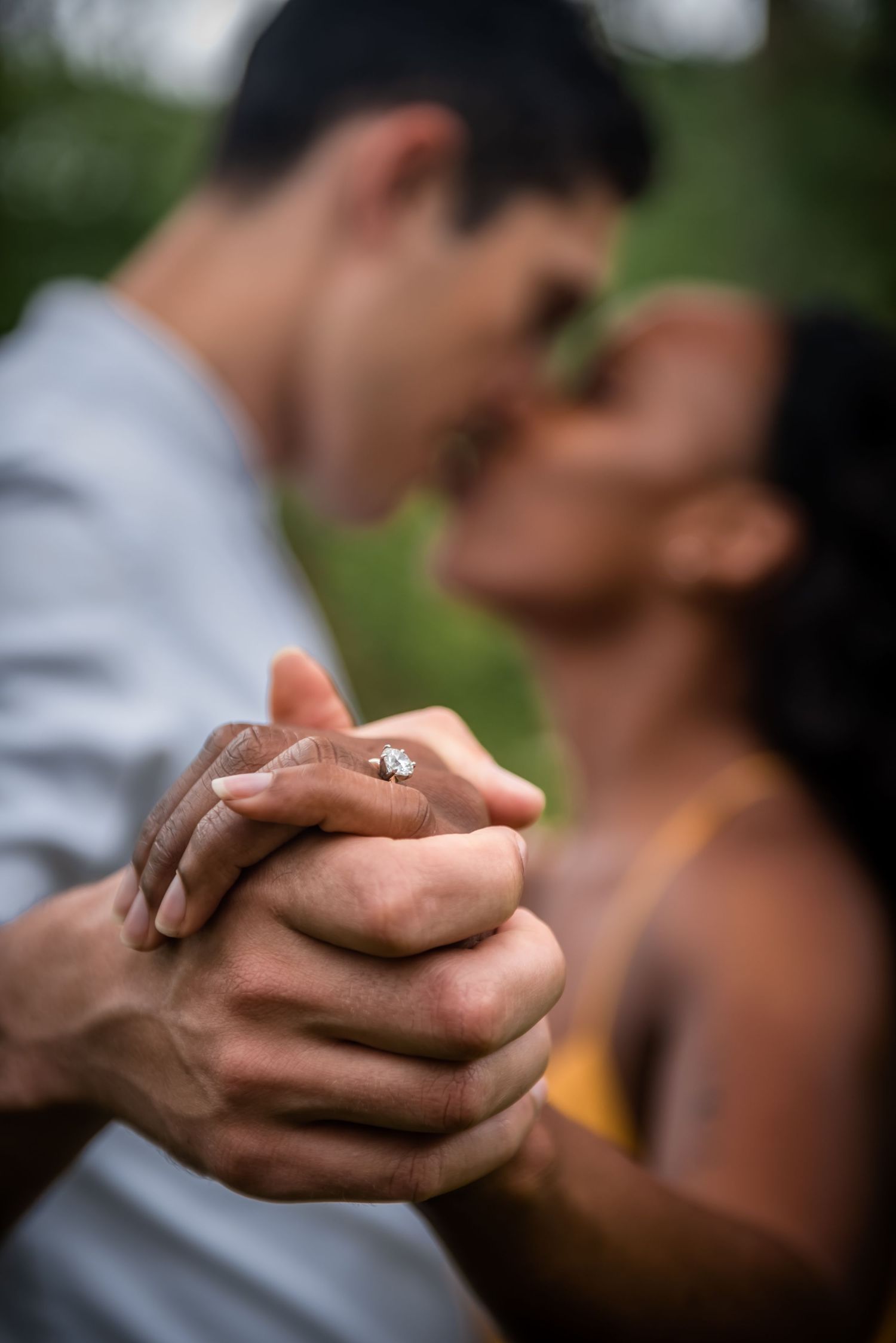 Close-up of a diamond engagement ring as two people share an intimate dance together outdoors.