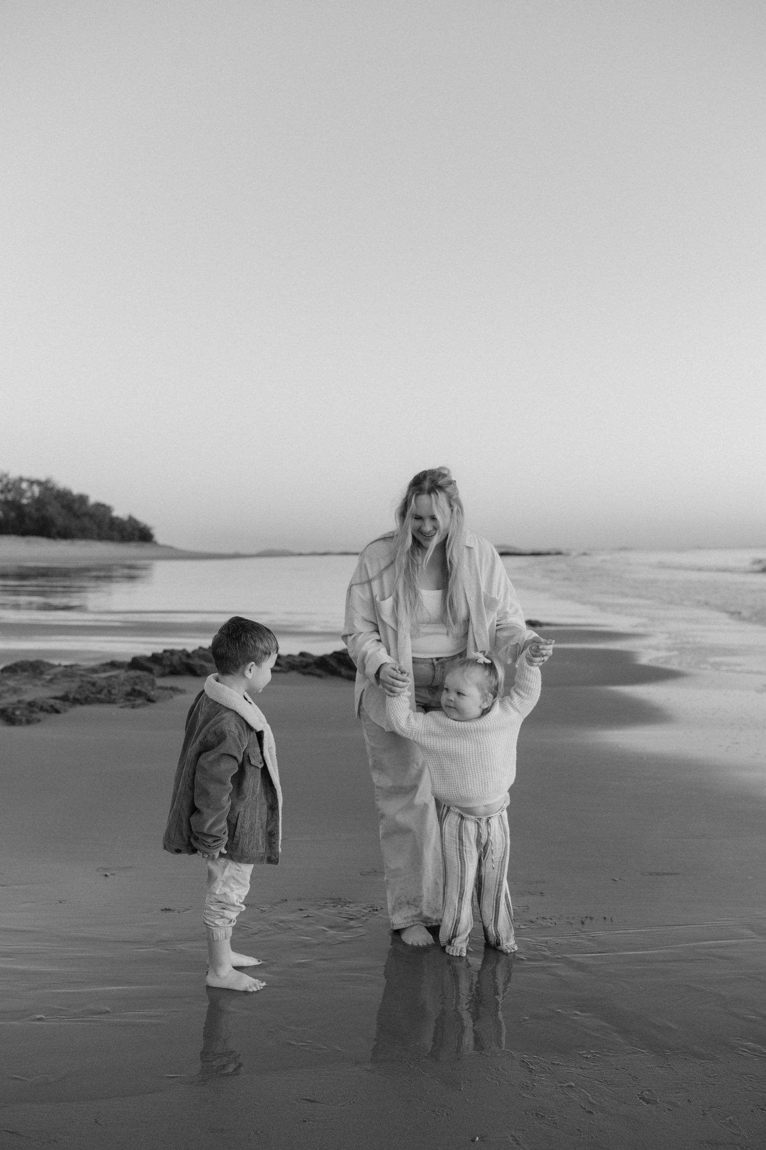 Black and white series of family photos on a beach showing interaction between small child and adult on a cloudy day.
