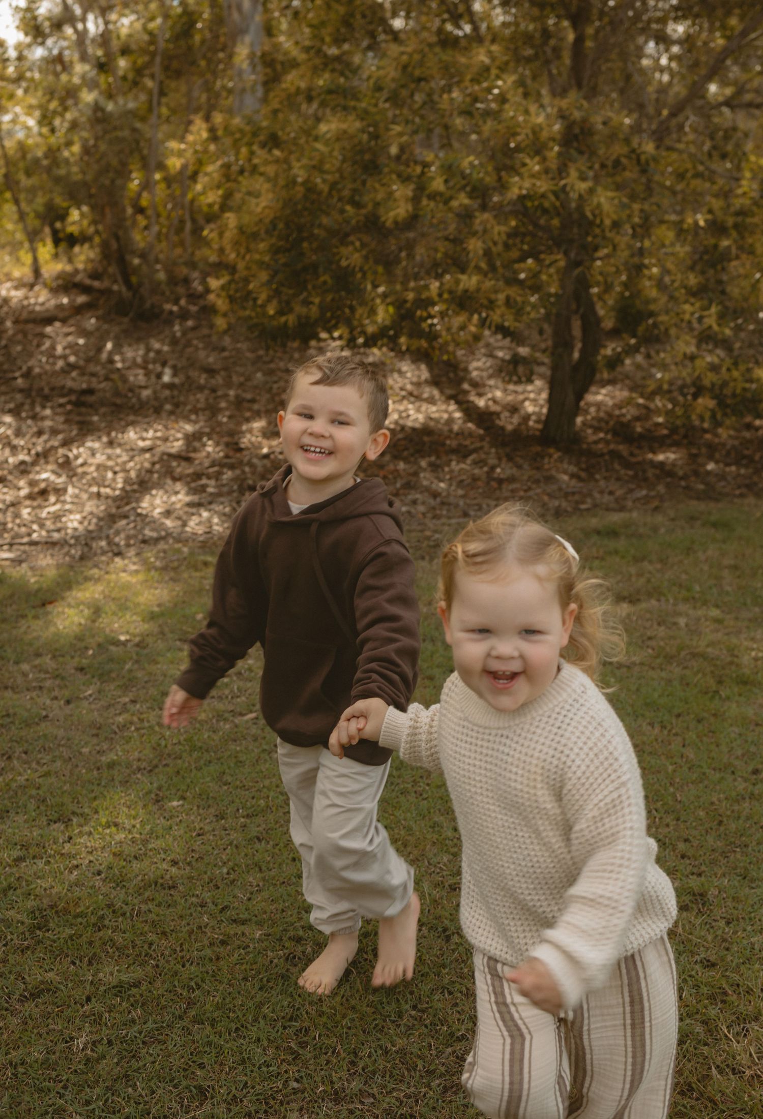 Two small children playing and laughing together outdoors in autumn with trees in the background.