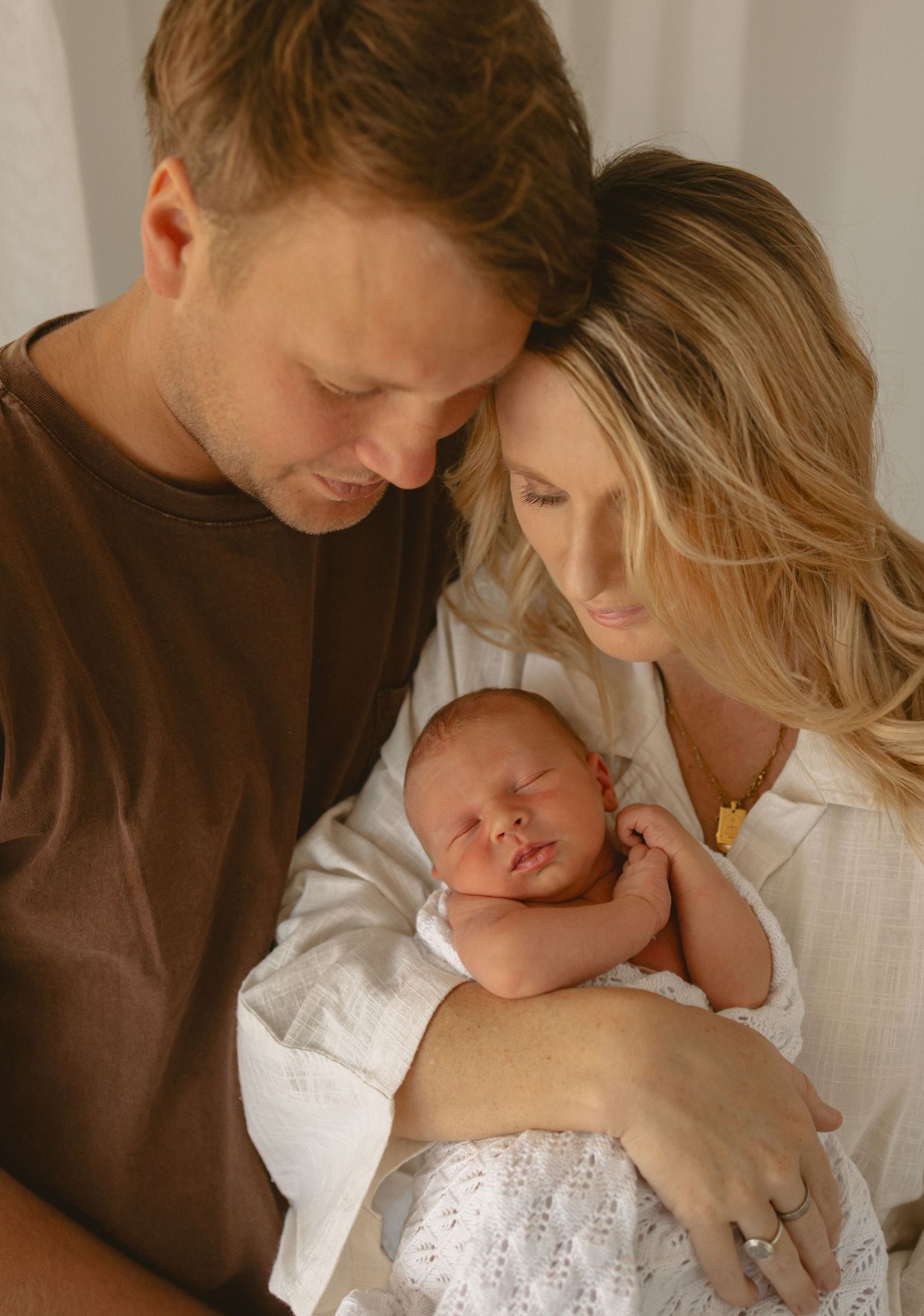 A tender family moment is captured as parents share an intimate embrace with their sleeping baby in soft lighting.