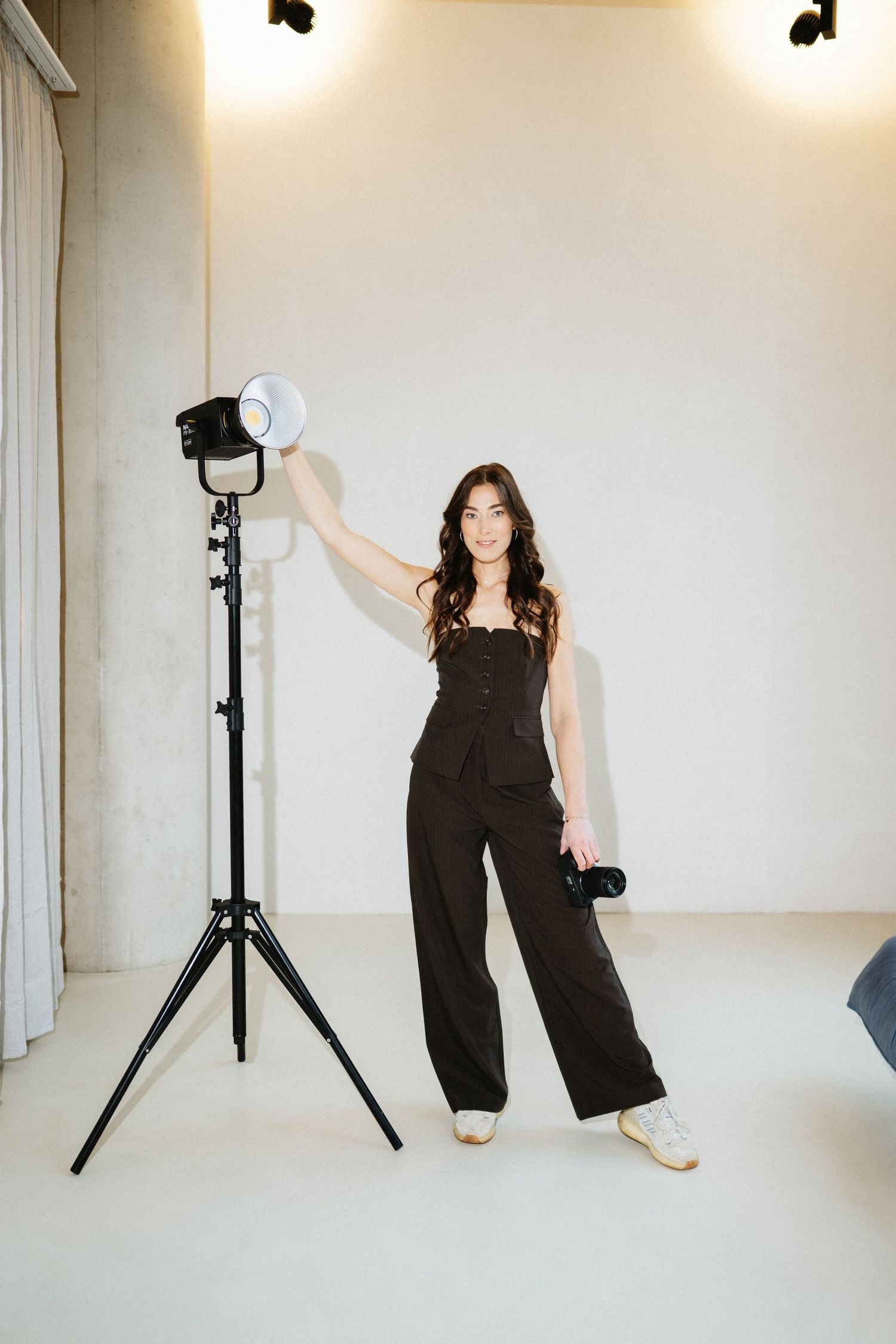 Studio photography session with person in black outfit against white backdrop and lighting equipment.