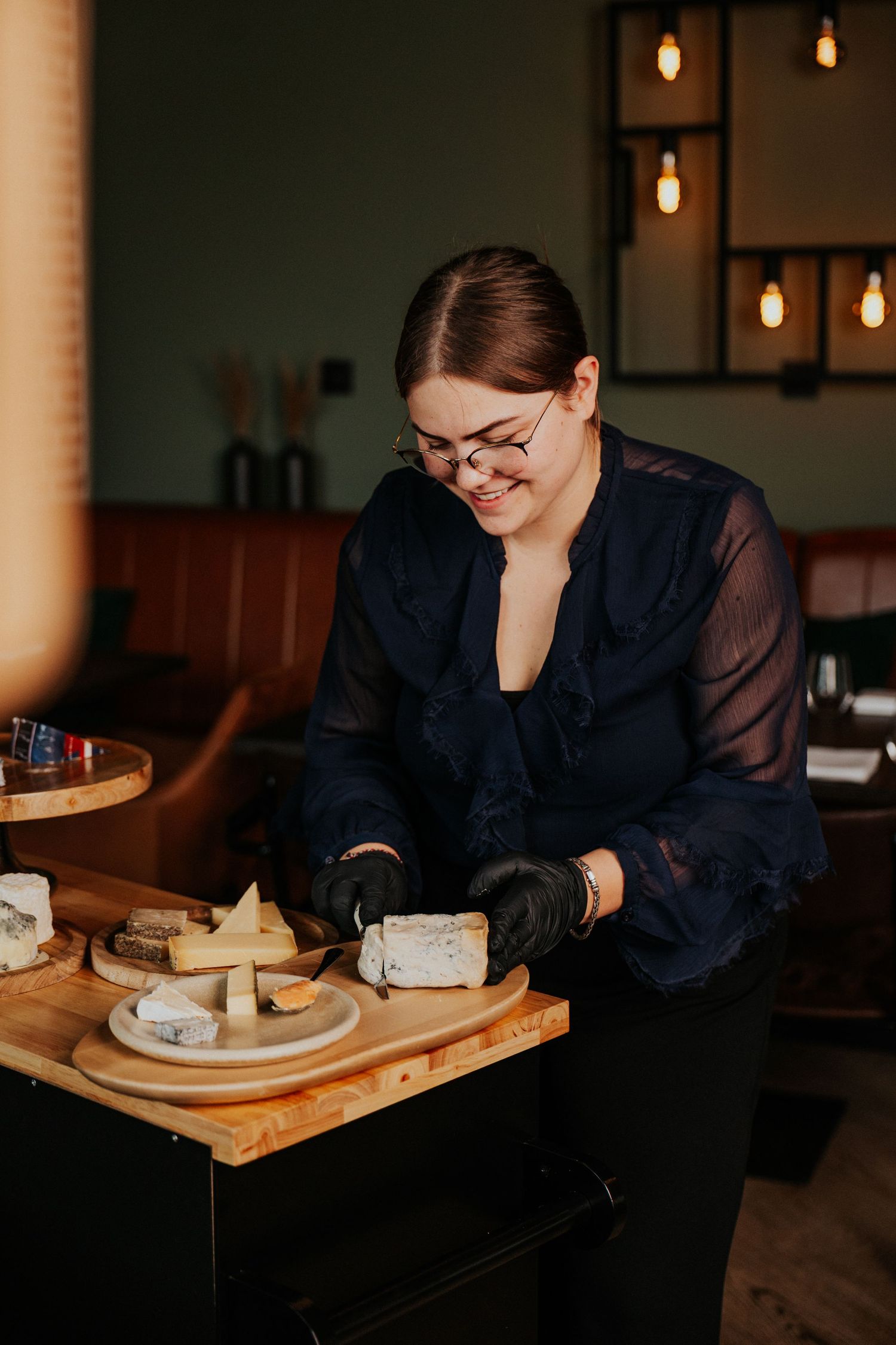 Moody restaurant scene with someone dining at a wooden table under warm pendant lighting.
