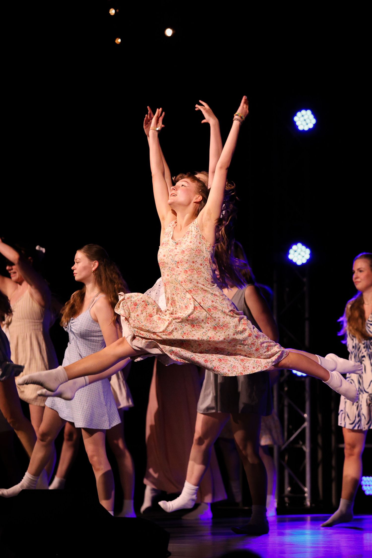 Dancers perform graceful leaps and movements on a dark stage illuminated by blue spotlights during a dance recital.