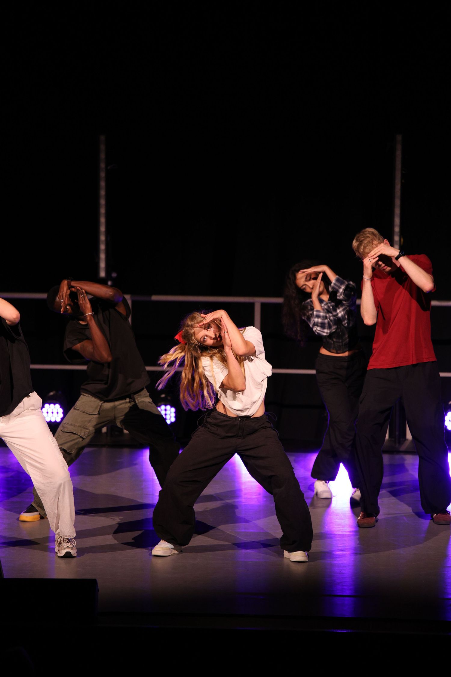 Dancers perform a synchronized hip-hop routine on a dark stage illuminated by blue lighting.