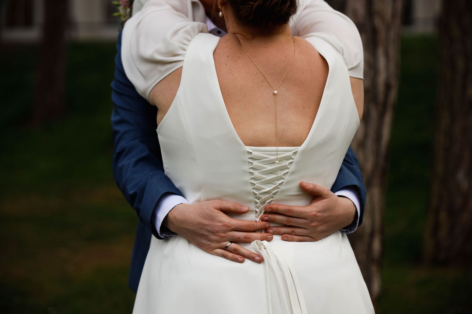 A close-up detail shot of a white wedding dress showing a corset-style back with satin ribbon lacing.