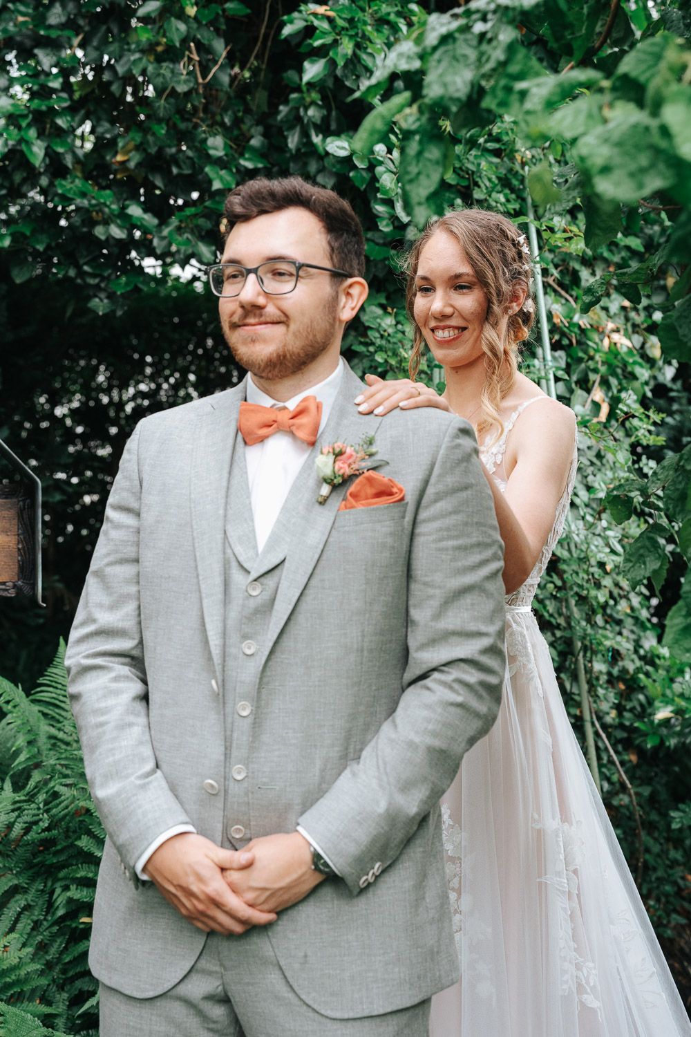 A couple shares joyful moments during their wedding first look in a lush green garden setting.