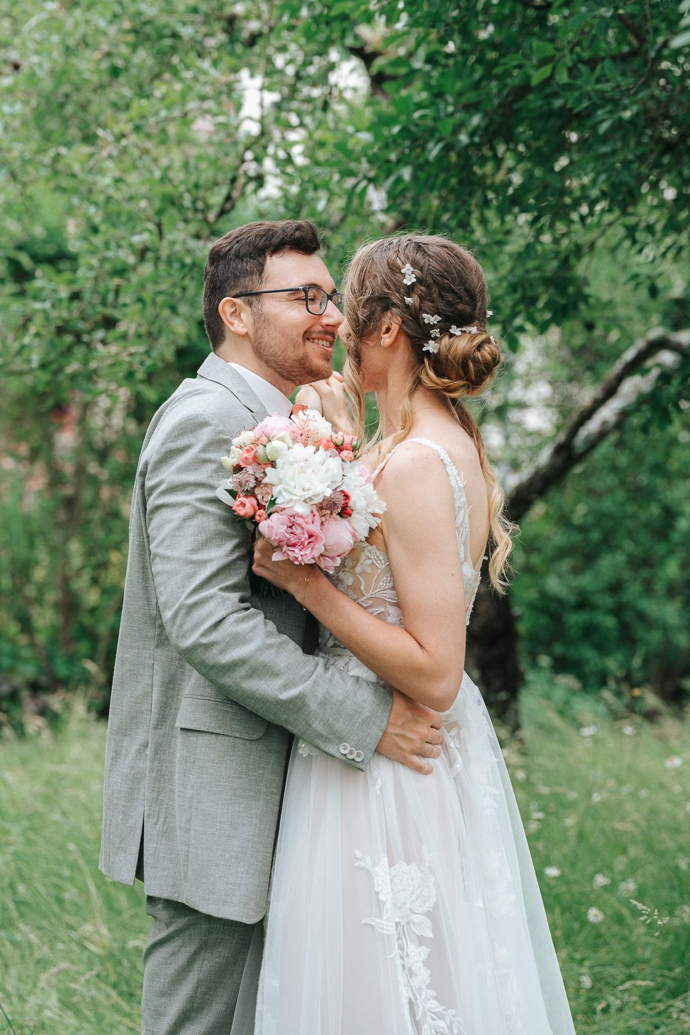 A romantic outdoor wedding photo features a couple embracing while holding a pink floral bouquet in a lush garden setting.