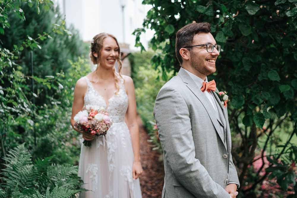 Wedding couple shares a candid laughing moment together surrounded by lush greenery in an outdoor garden setting.