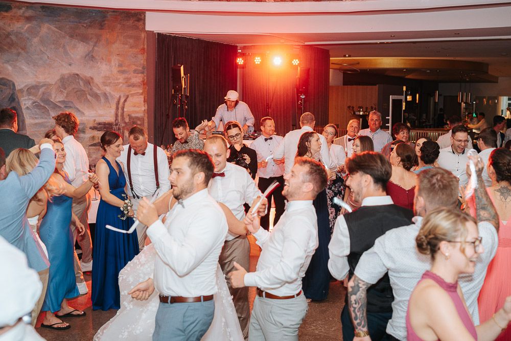 Wedding reception guests dance together in a ballroom with red lighting creating a festive party atmosphere.