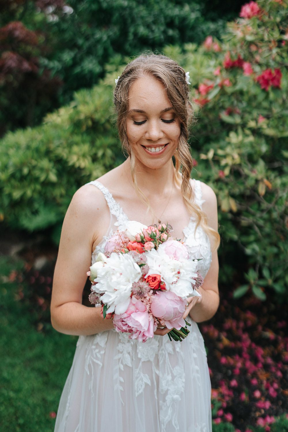Soft white wedding dress with delicate floral details and a pink peony bouquet in a garden.