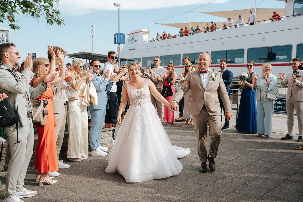 Wedding party and guests enjoying a lively dance celebration on an outdoor deck overlooking mountains and water.