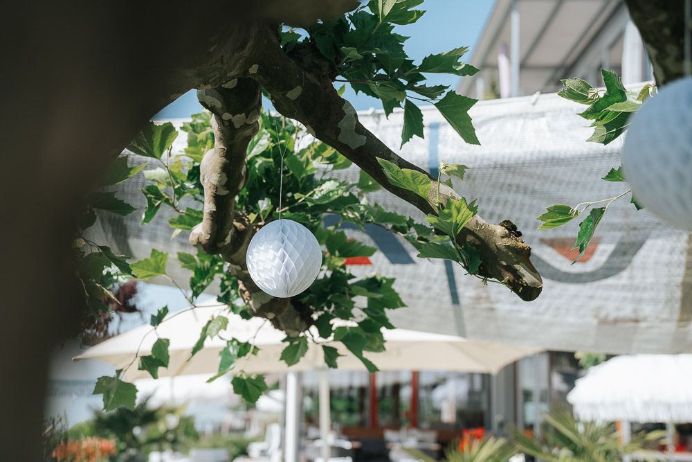 String lights and hanging white lanterns decorate an outdoor wedding reception area under a clear canopy tent.