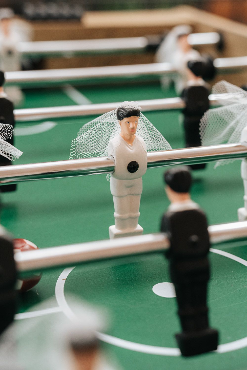 Close-up shot of a white foosball figure wearing a small veil surrounded by other players on a green table.