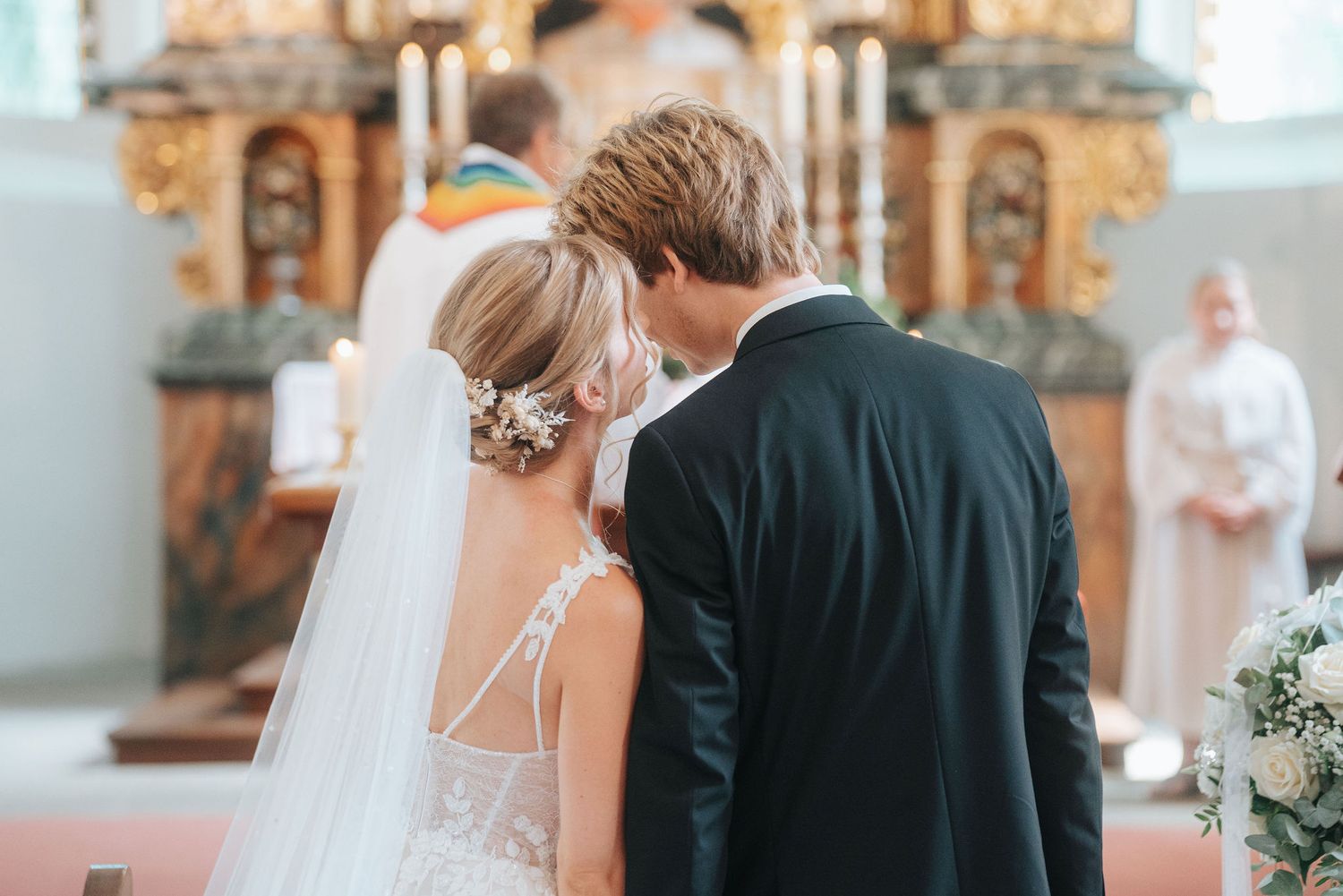 Bride and groom standing at church altar during wedding ceremony, bride wearing white gown and veil.