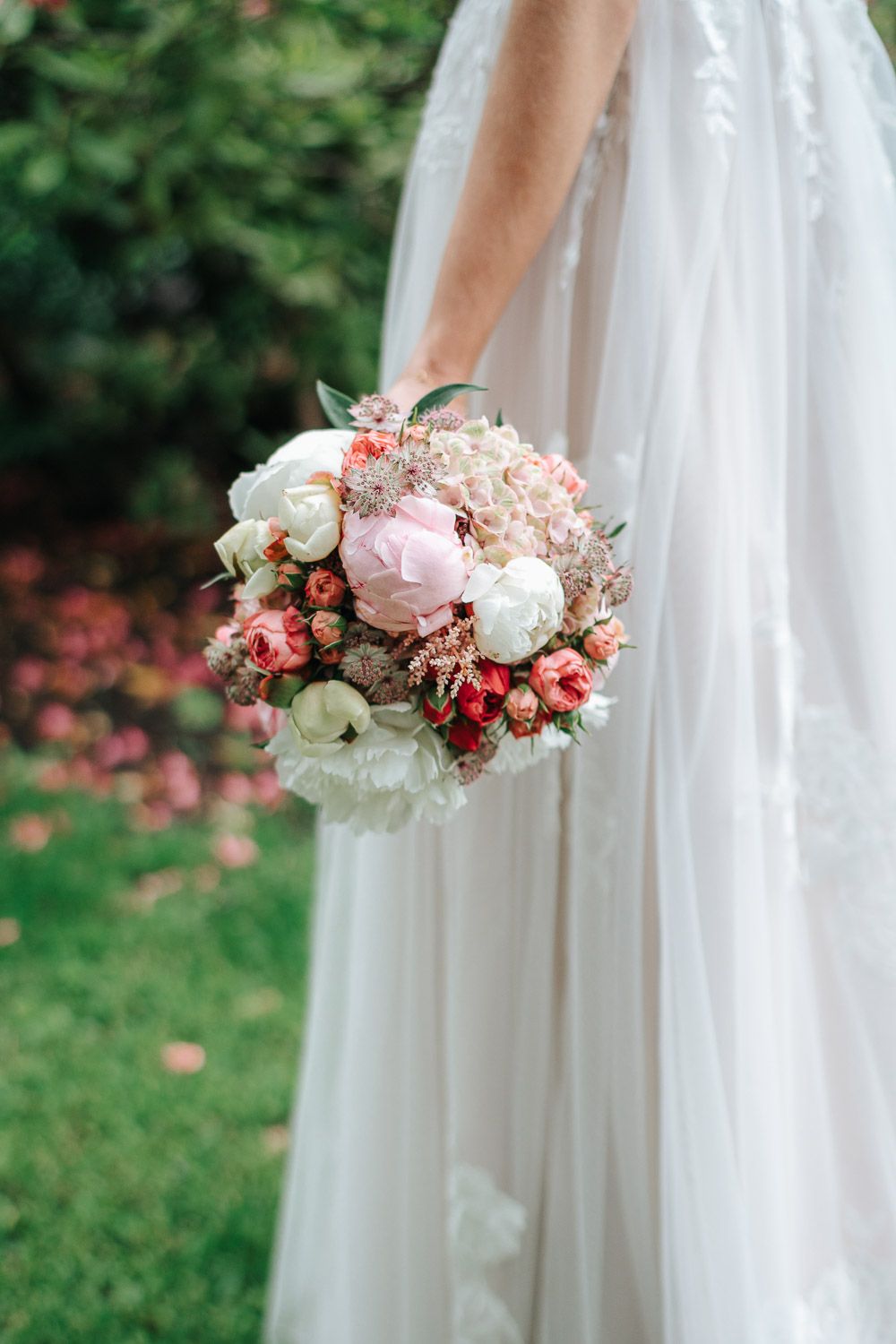 A romantic bridal bouquet with pink and white roses against a flowing white wedding dress in a garden setting.