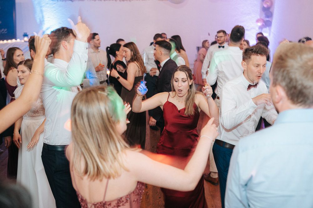 Group of party guests dancing energetically at a reception with color-changing lights in background.