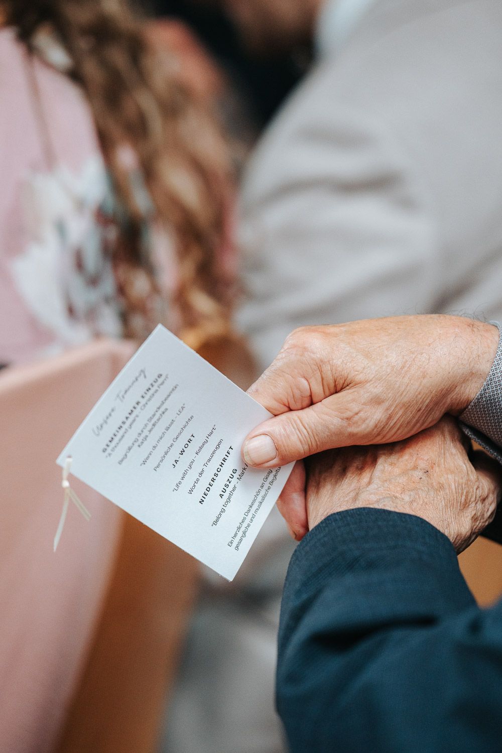 Close-up shot of hands holding a small white card or note during what appears to be a formal occasion.