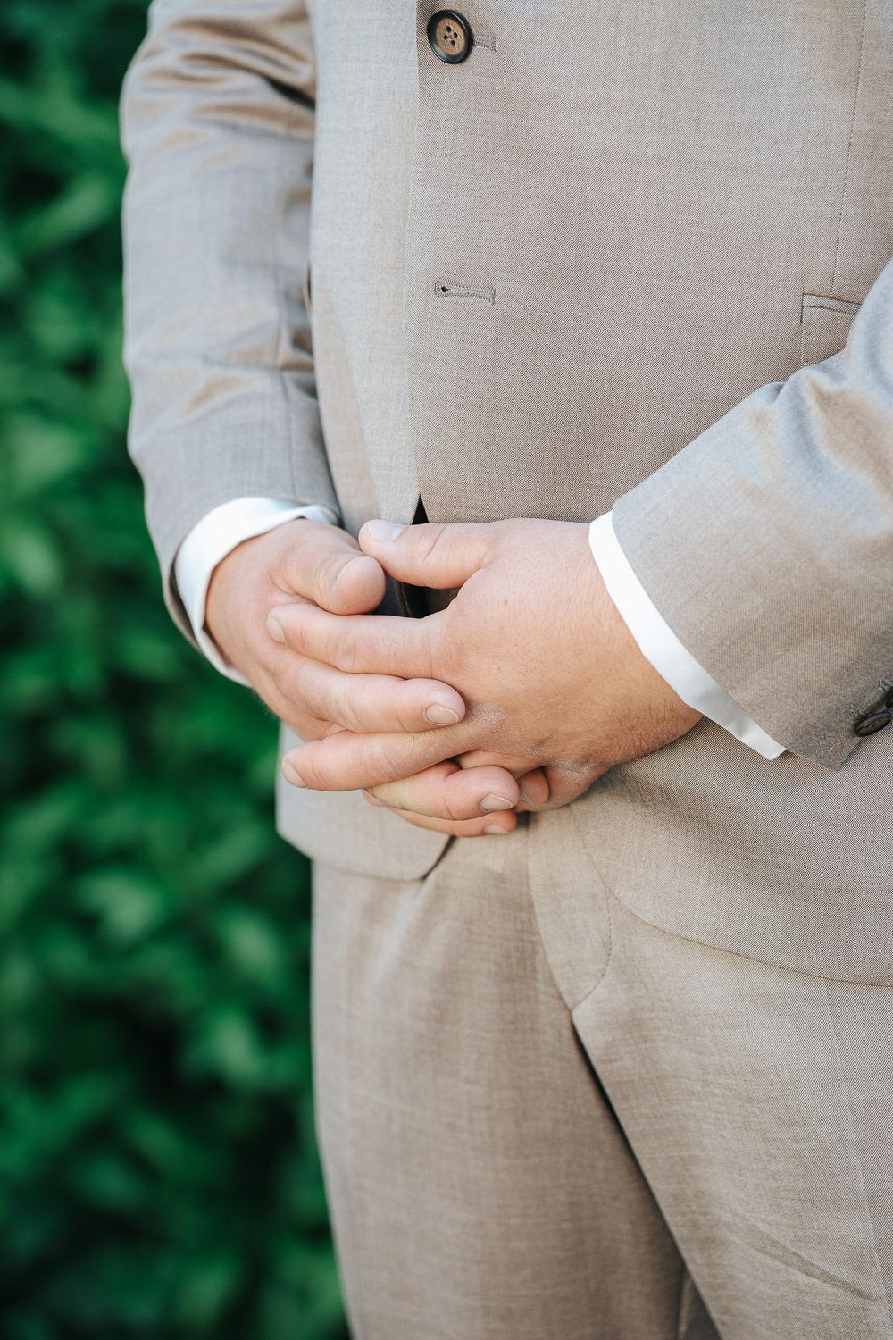 Close-up of clasped hands wearing a beige linen suit against a soft green background.