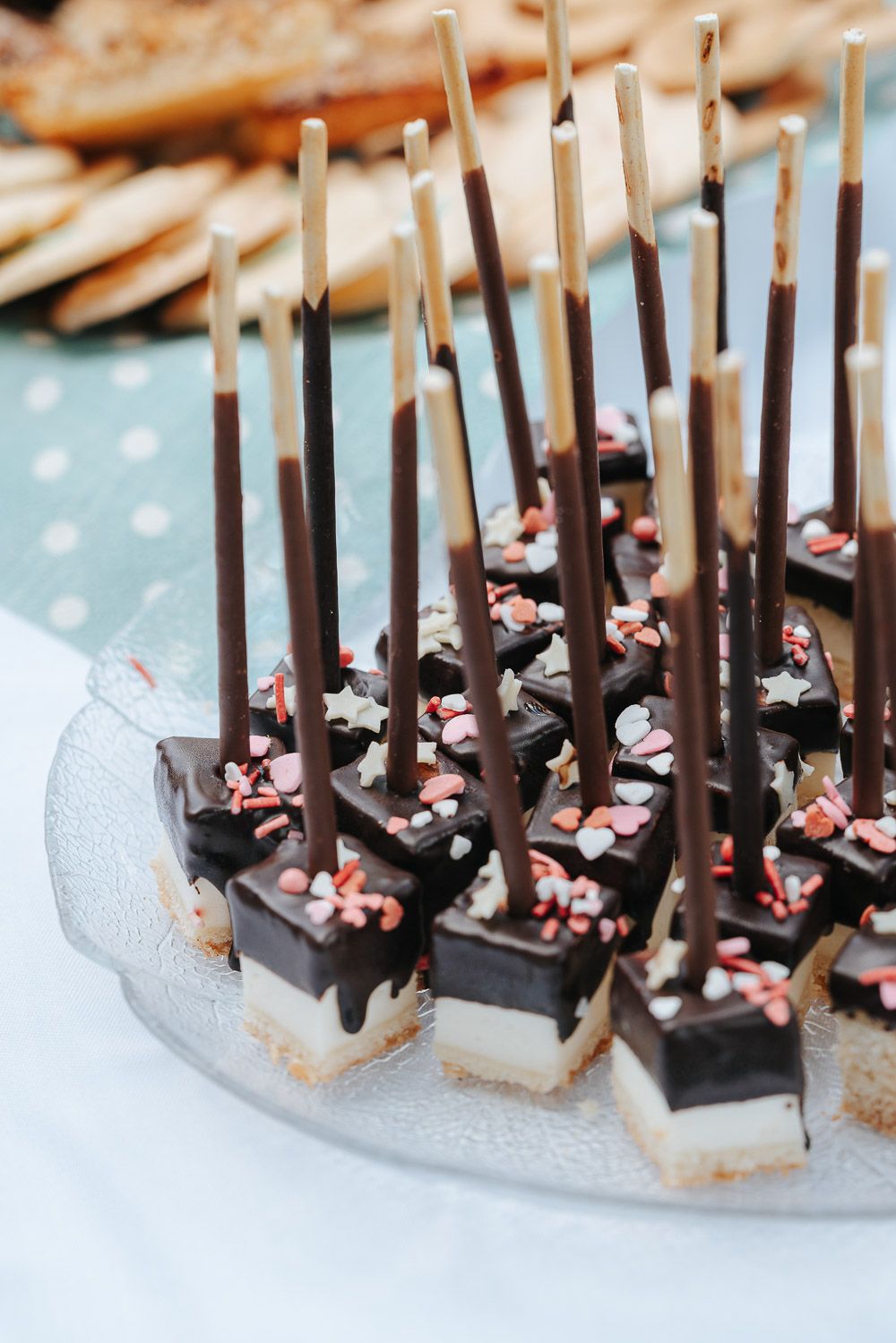 Chocolate-covered cheesecake bites decorated with peppermint candies and dark sticks on a polka dot tablecloth.