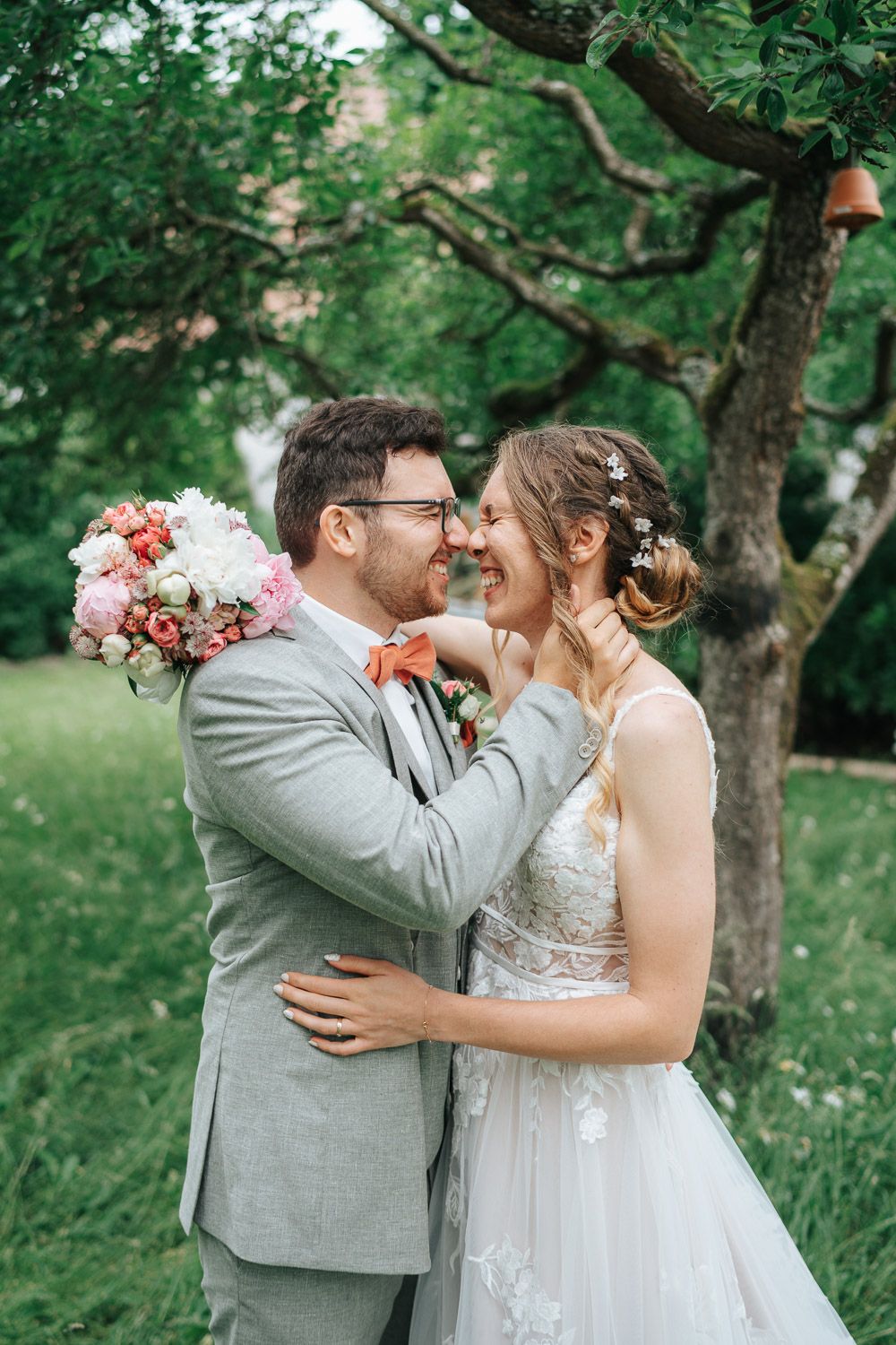 A joyful newlywed couple share an intimate moment in a lush garden setting with pink floral bouquet.