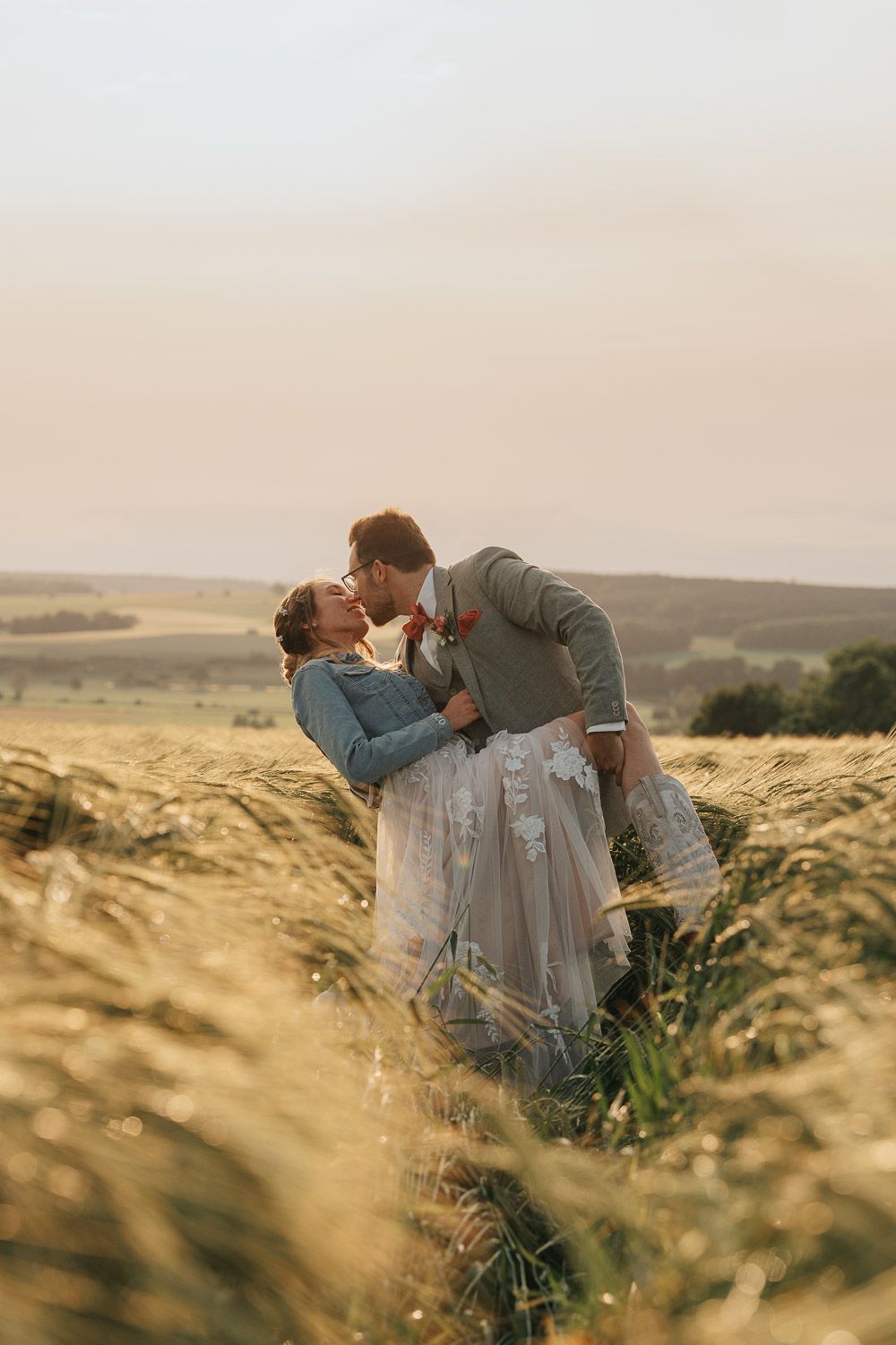 Romantic couple embrace in a golden wheat field at sunset creating a dreamy ethereal atmosphere.