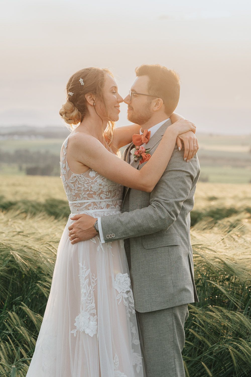 Newlyweds share an intimate moment in a windy wheat field at sunset.
