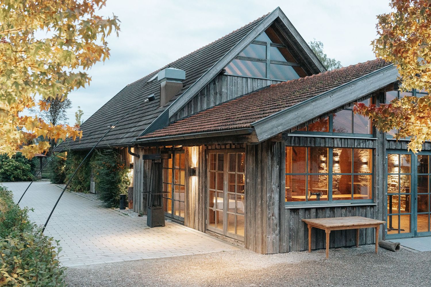 Modern wooden cabin with large windows nestled among autumn trees in a snowy mountain setting.