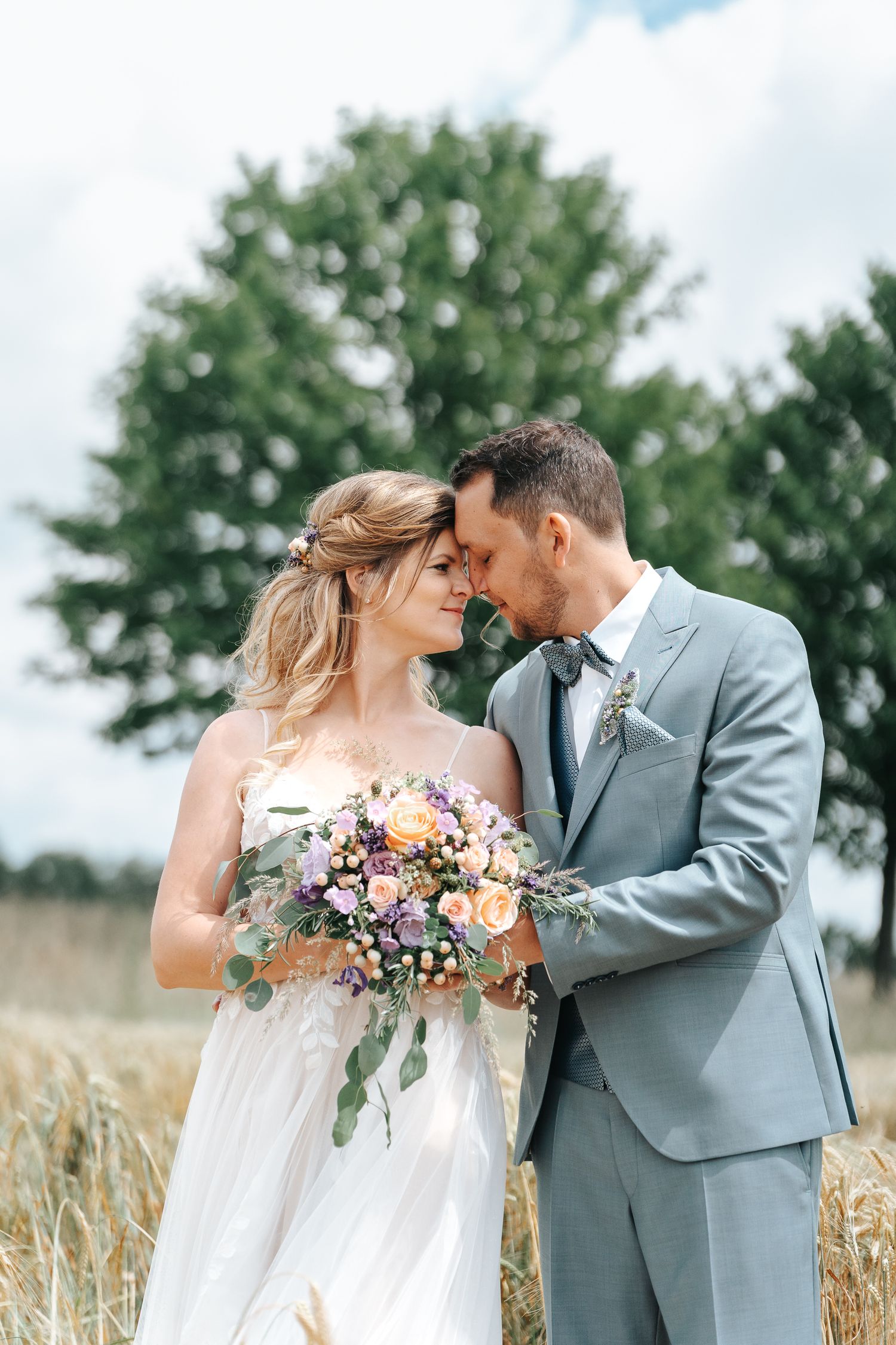 A romantic wedding portrait of a couple sharing an intimate moment in a wheat field with a beautiful bouquet.