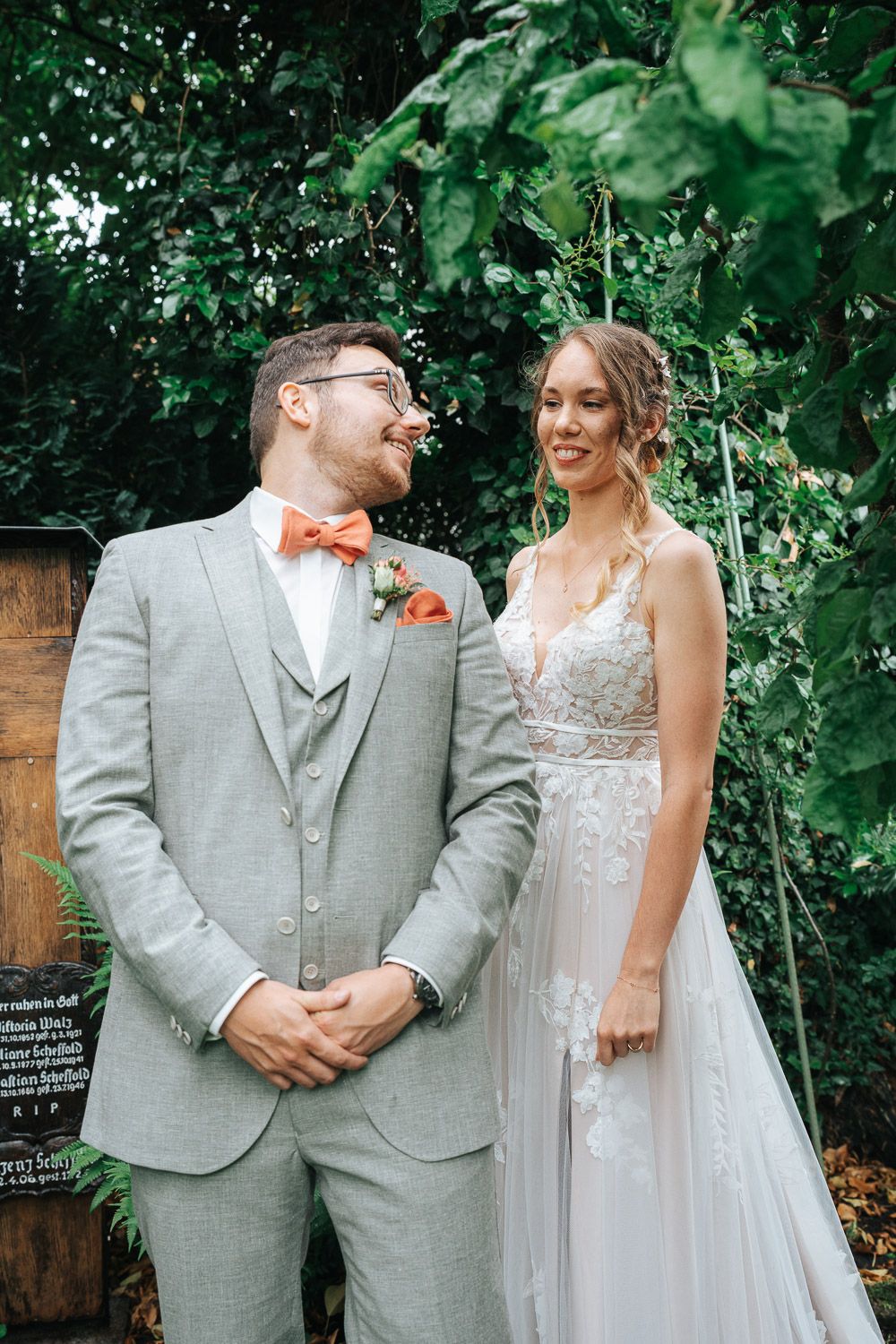 Newlywed couple share joyful moments together in garden setting wearing gray suit and white lace dress with orange accents.